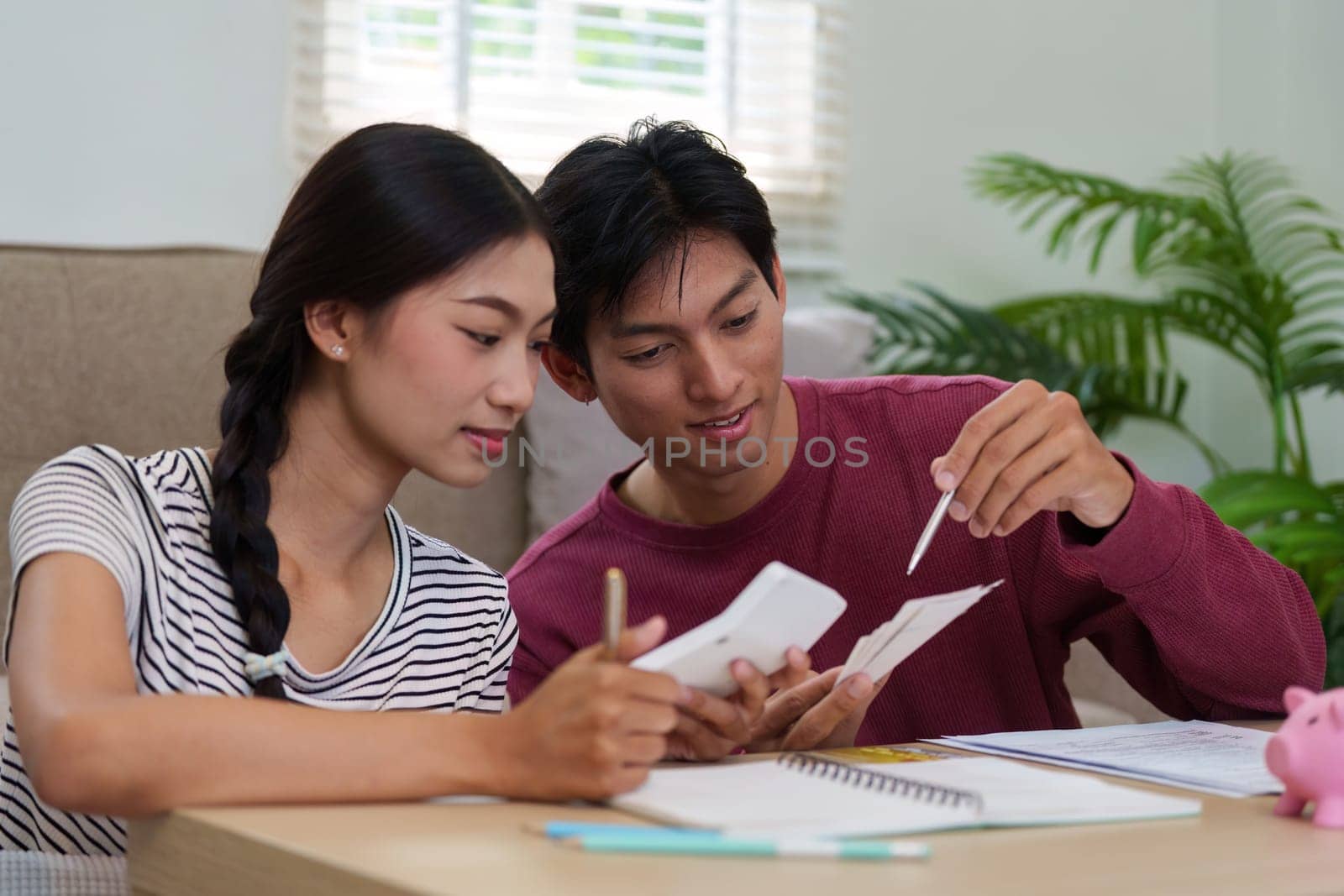A young couple sits together, discussing their financial planning and budgeting strategies while using worksheets and a calculator, indicating their commitment to financial growth.