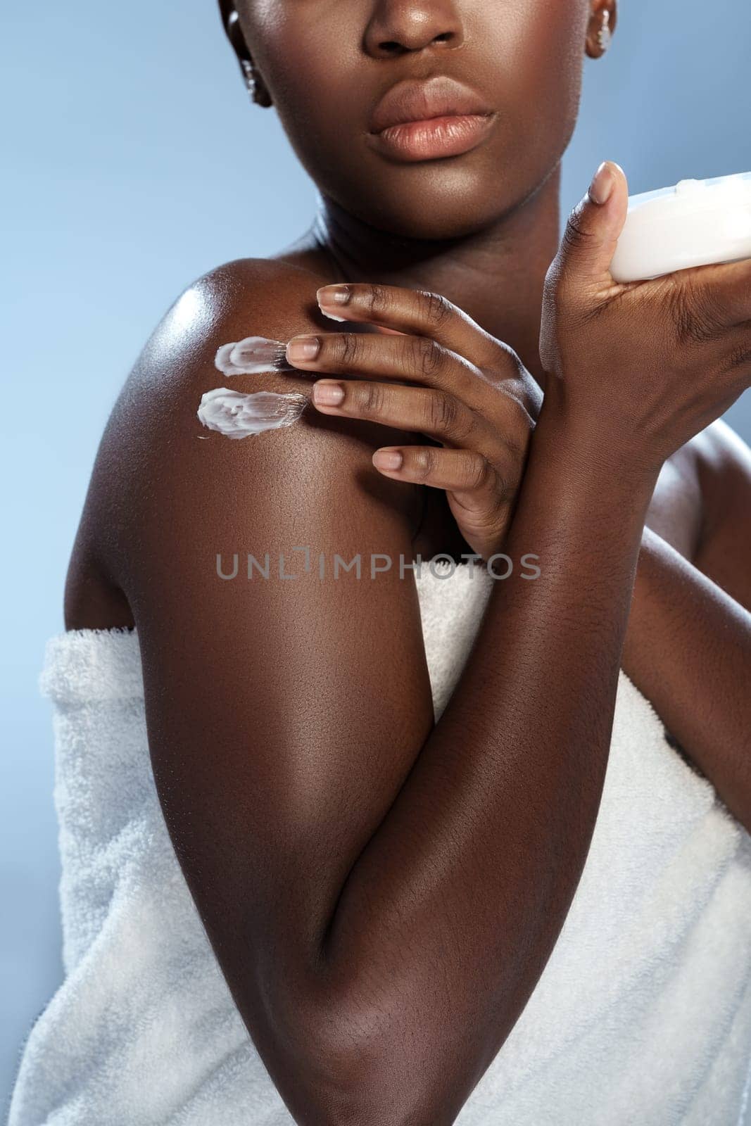 A person is gently applying moisturizing cream on their shoulder, wrapped in a towel, showcasing a self-care routine. The soft light reflects on their skin, emphasizing hydration.