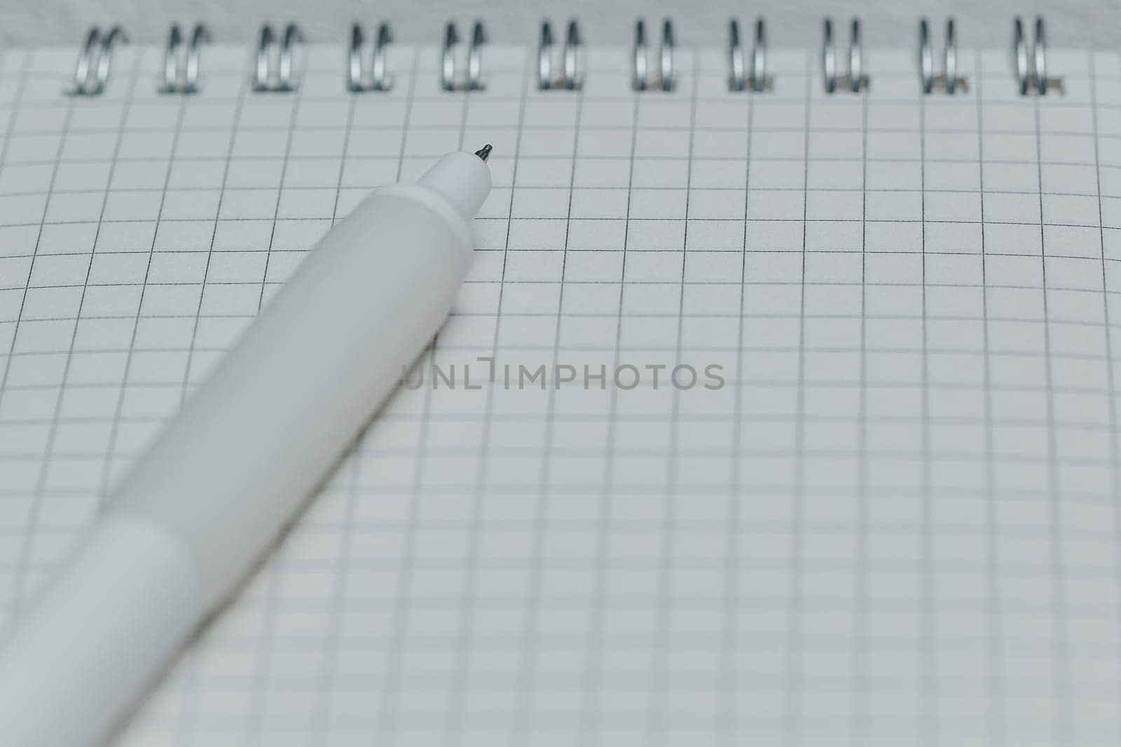 Close-up of white pen tip on grid notebook page. Concept of writing, note-taking, planning, education, stationery, and creative workspace.