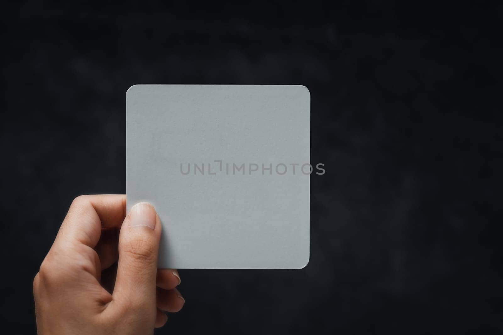 Woman's hand holding white note against black background. Concept of message, communication, minimal design, announcement, and copy space for text or branding.