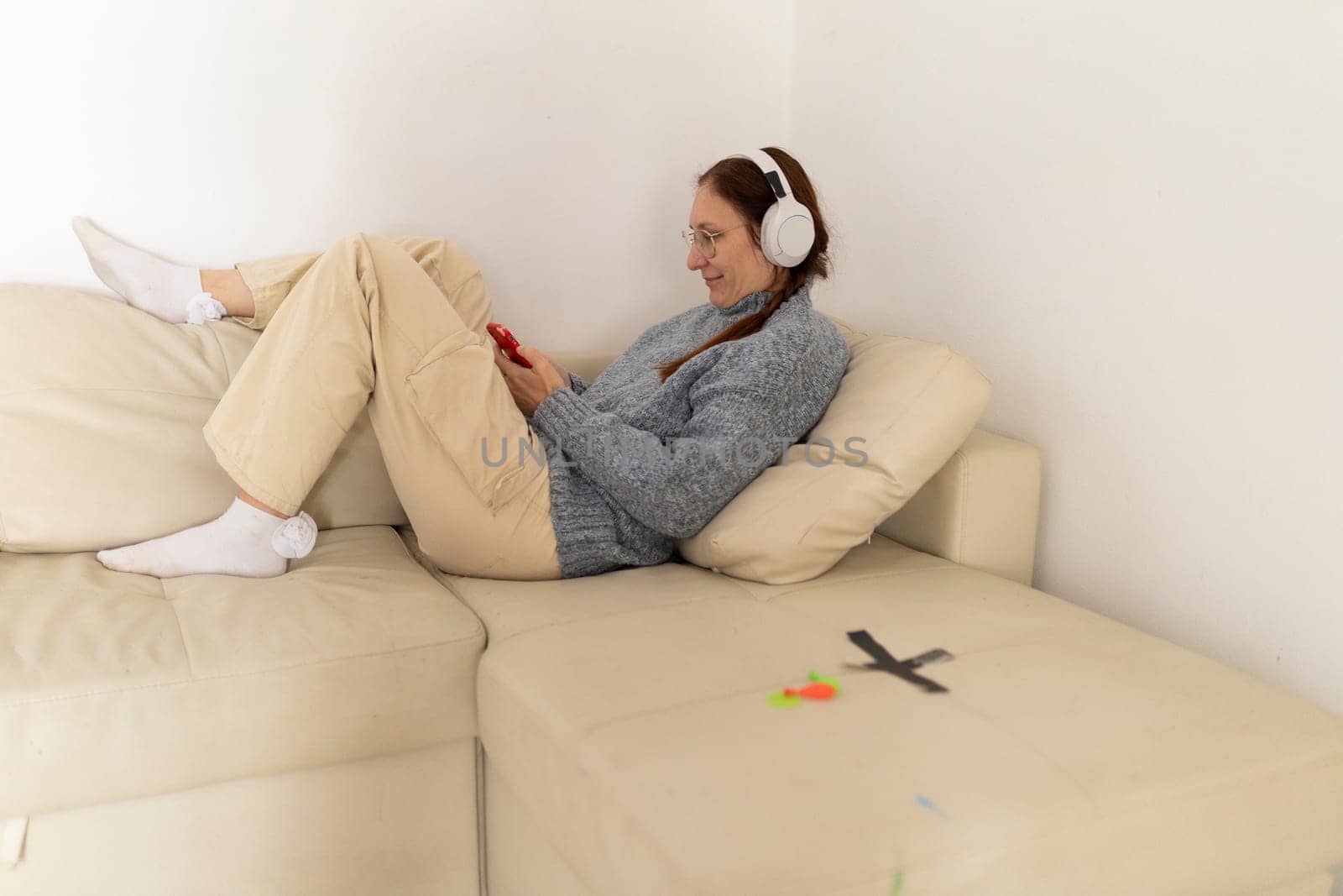 Mature woman enjoying music with headphones while using smartphone on a comfortable sofa at home