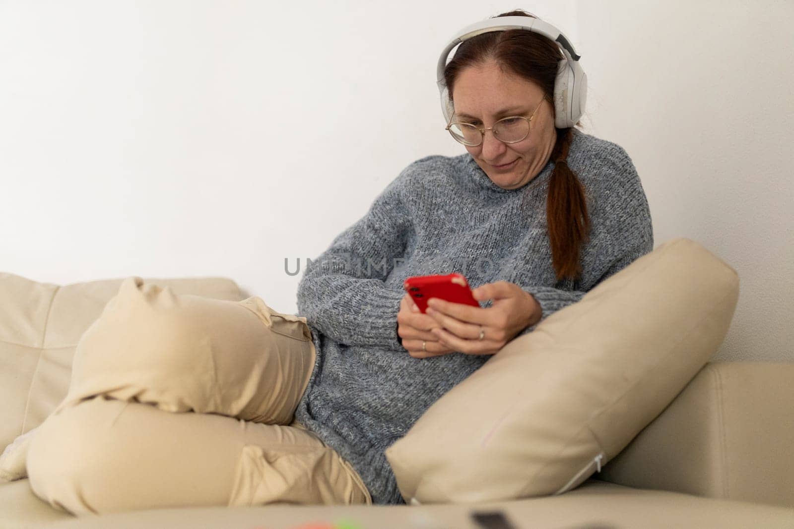 Woman wearing headphones and using smartphone while relaxing on a comfortable sofa at home