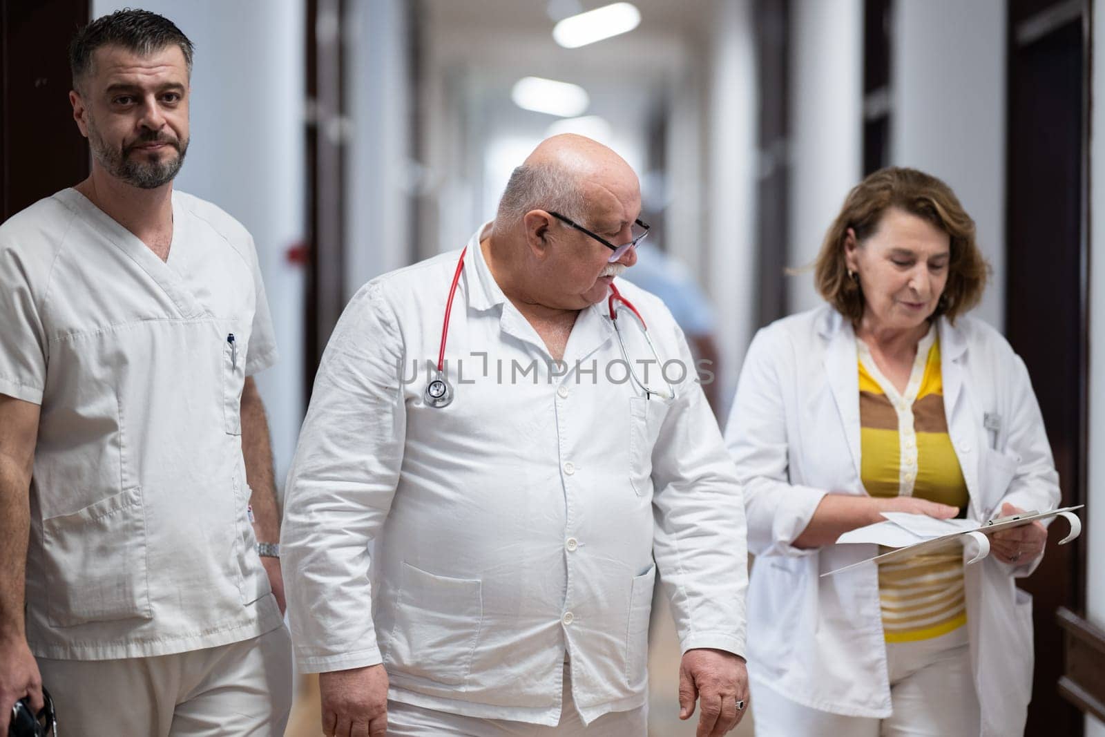 A group of healthcare professionals in white uniforms walking through a hospital hallway while reviewing patient documents and discussing treatment plans