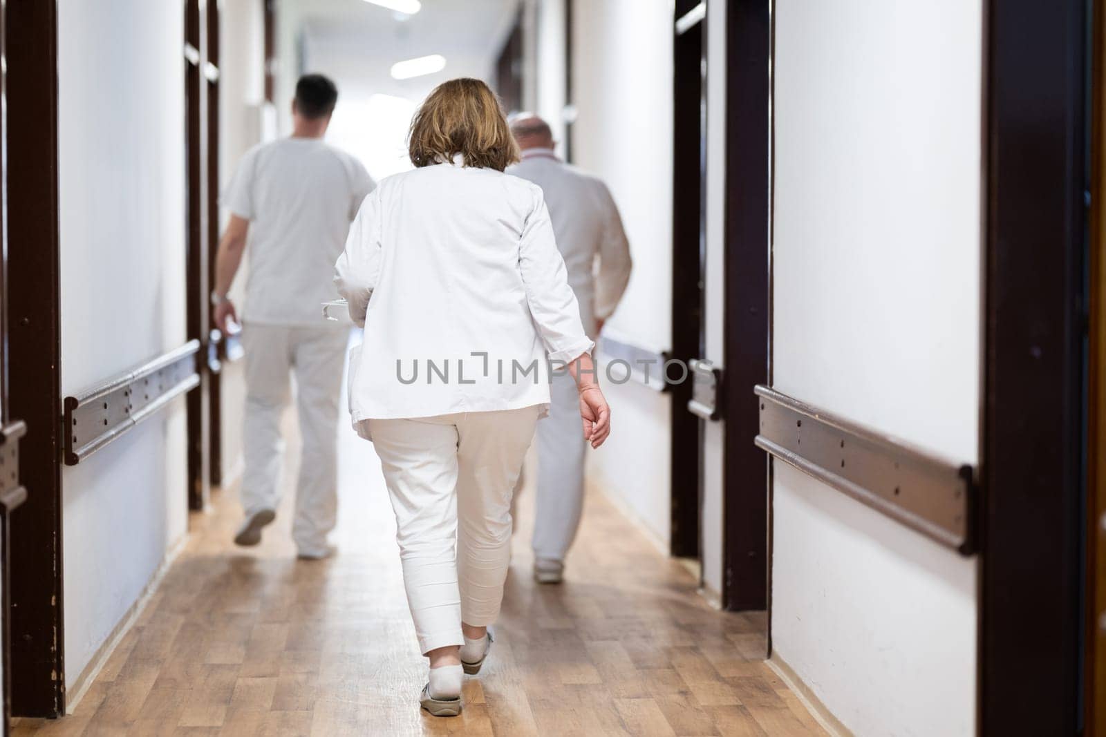 A group of healthcare professionals in white uniforms walking through a hospital hallway while reviewing patient documents and discussing treatment plans
