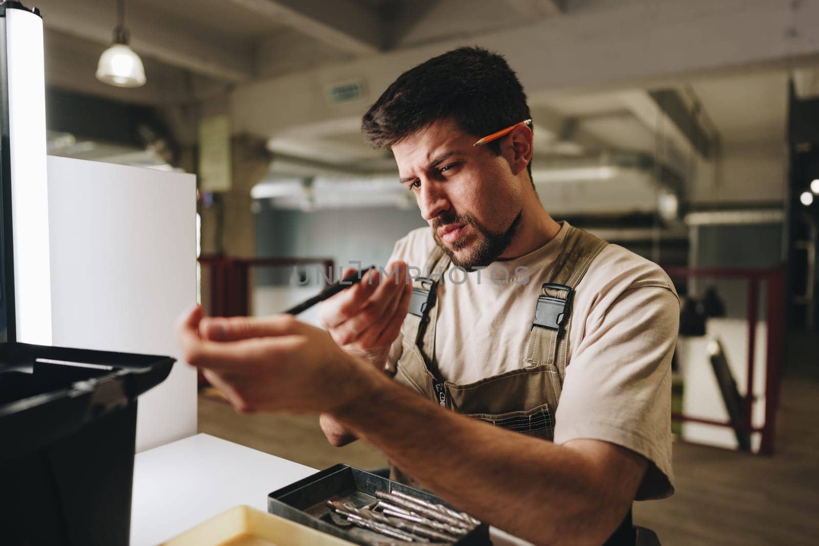 A skilled craftsman examines a tool closely while working in a well-lit workshop. Focused and methodical, he ensures precision in his craft during the afternoon hours.