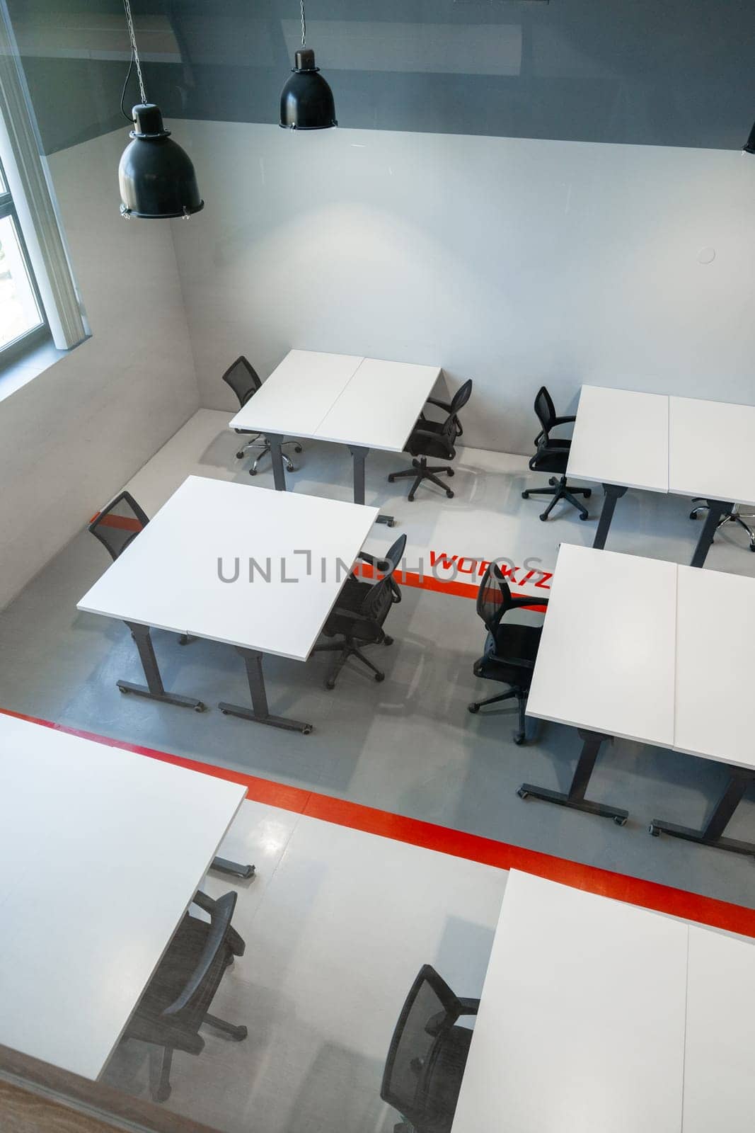 Bright coworking area featuring clean, white tables and comfortable black chairs. The space has a minimalist design, ideal for collaboration and productivity.