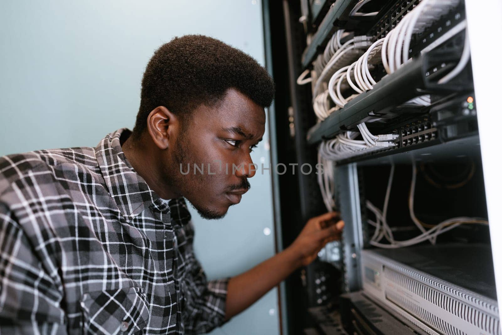 A technician works meticulously on organizing network cables within a server rack. This activity takes place in a tech facility during the evening, ensuring optimal management.