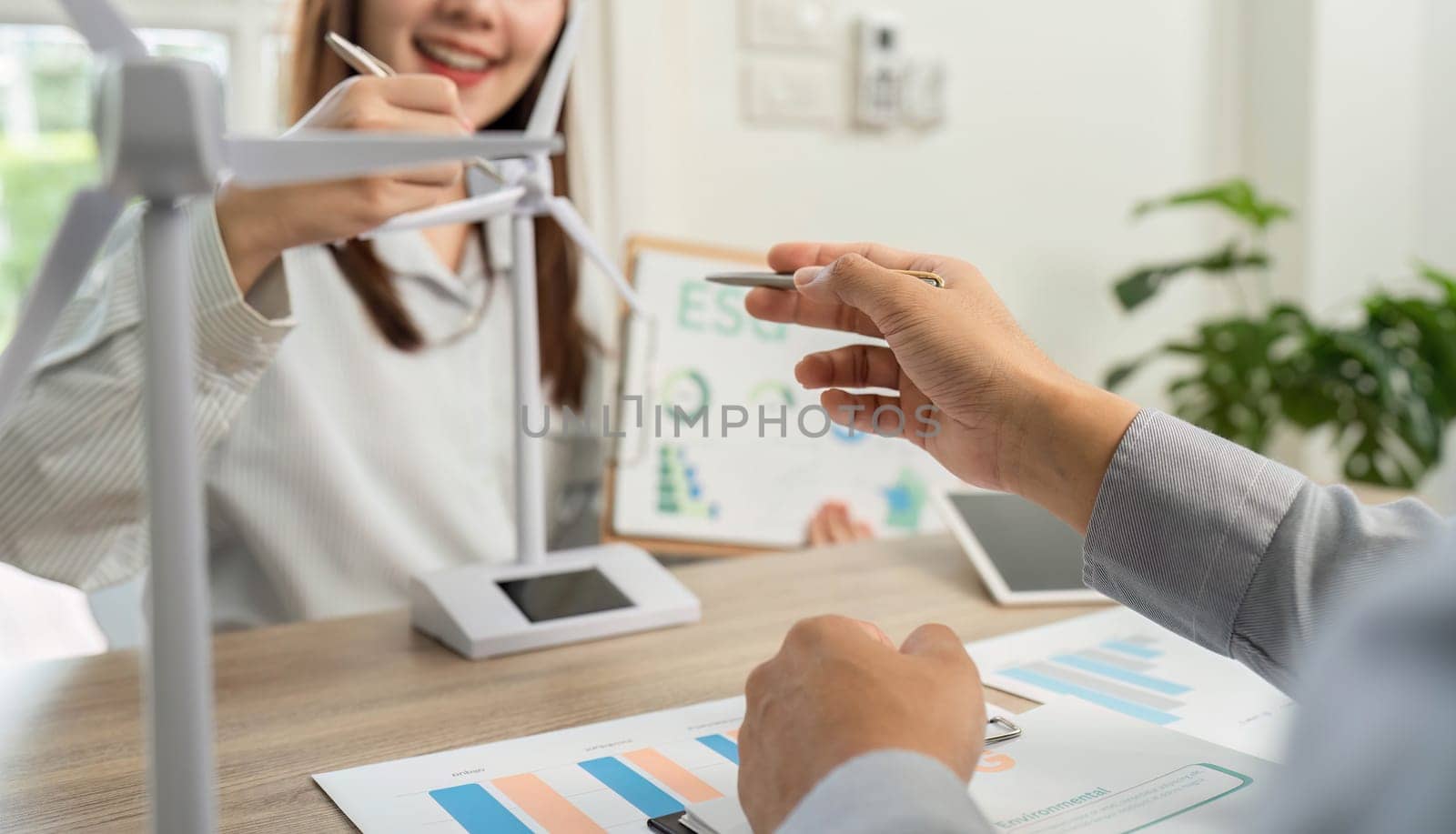 Two business professionals engaging in an ESG-focused discussion, analyzing sustainability metrics with a wind turbine model on the table.