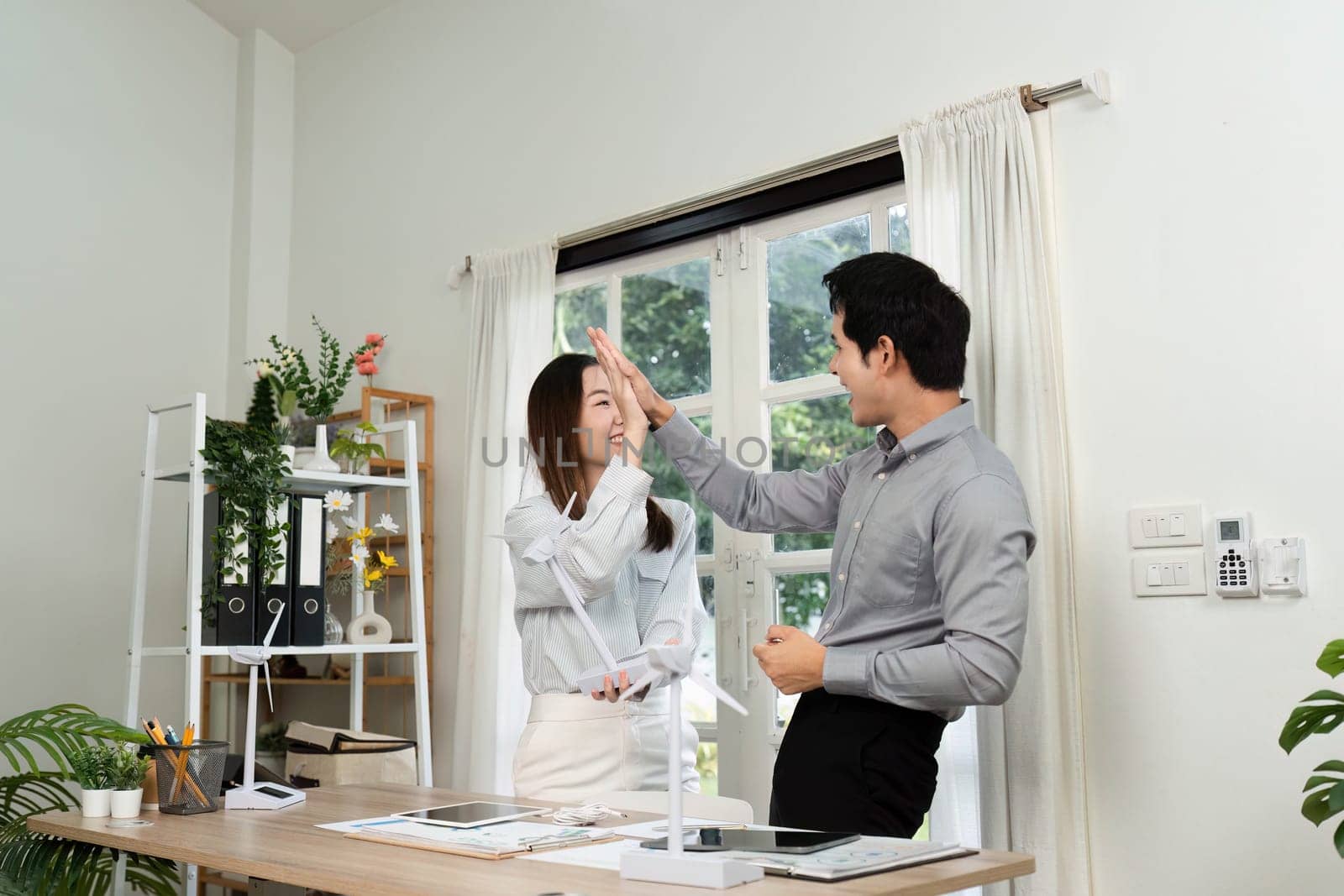 Two business professionals share a high-five, reflecting teamwork and enthusiasm for ESG initiatives in their workspace.