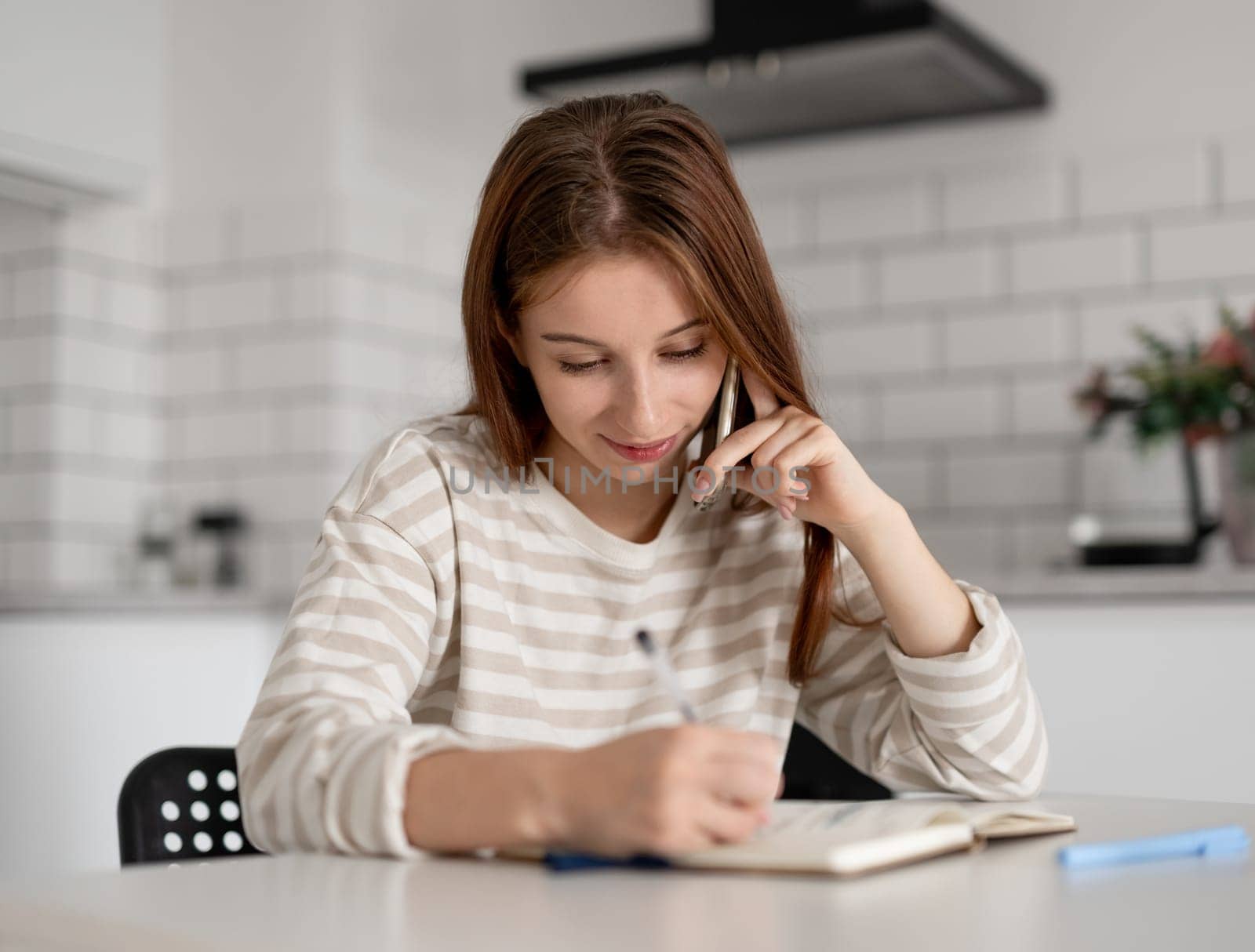 Girl Talks On Phone And Writes In Notebook At Home