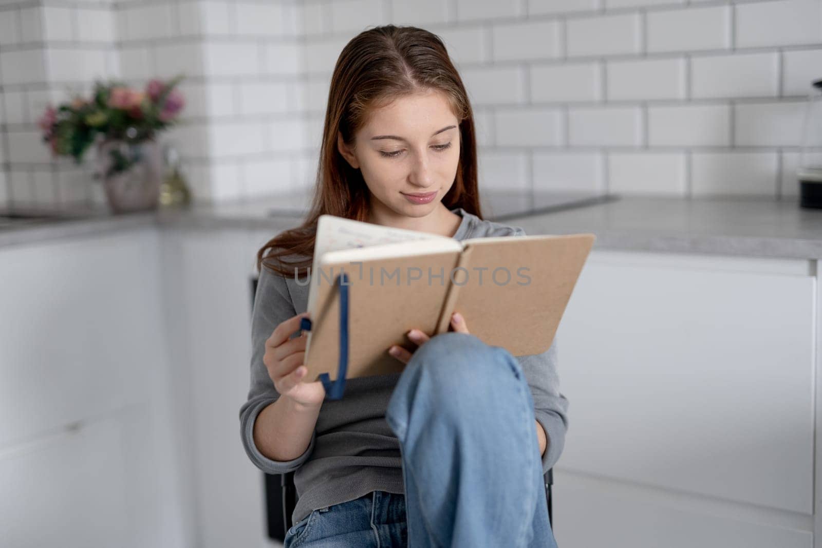 Sweet Teen Girl Reading Notebook Entries While Sitting On A Chair At Home