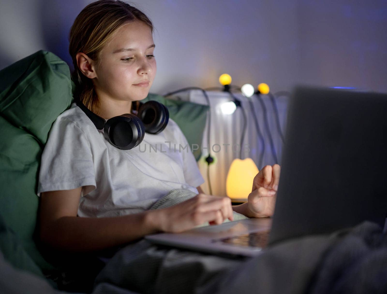 Cute Little Girl Browses The Internet And Social Media and Searching on laptop In Bed Before Sleep