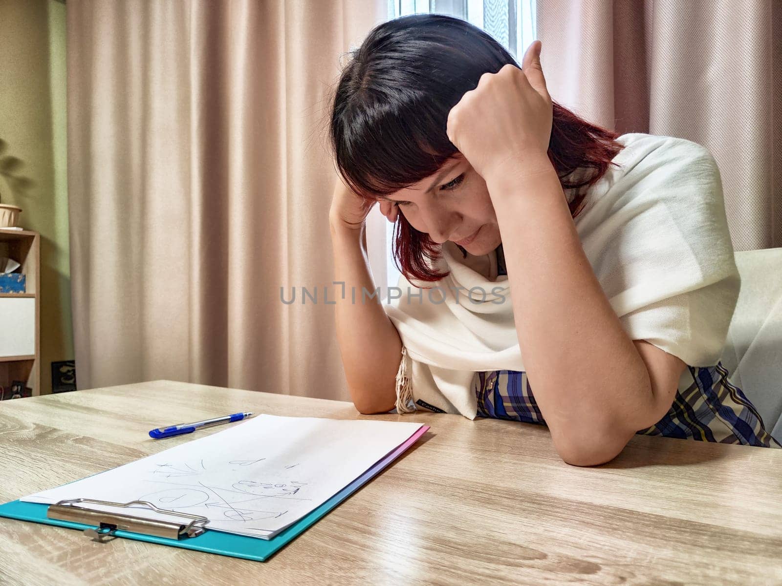 Middle-aged woman psychologist sits in her office with a thoughtful expression, reflecting on client notes and ideas during a session.