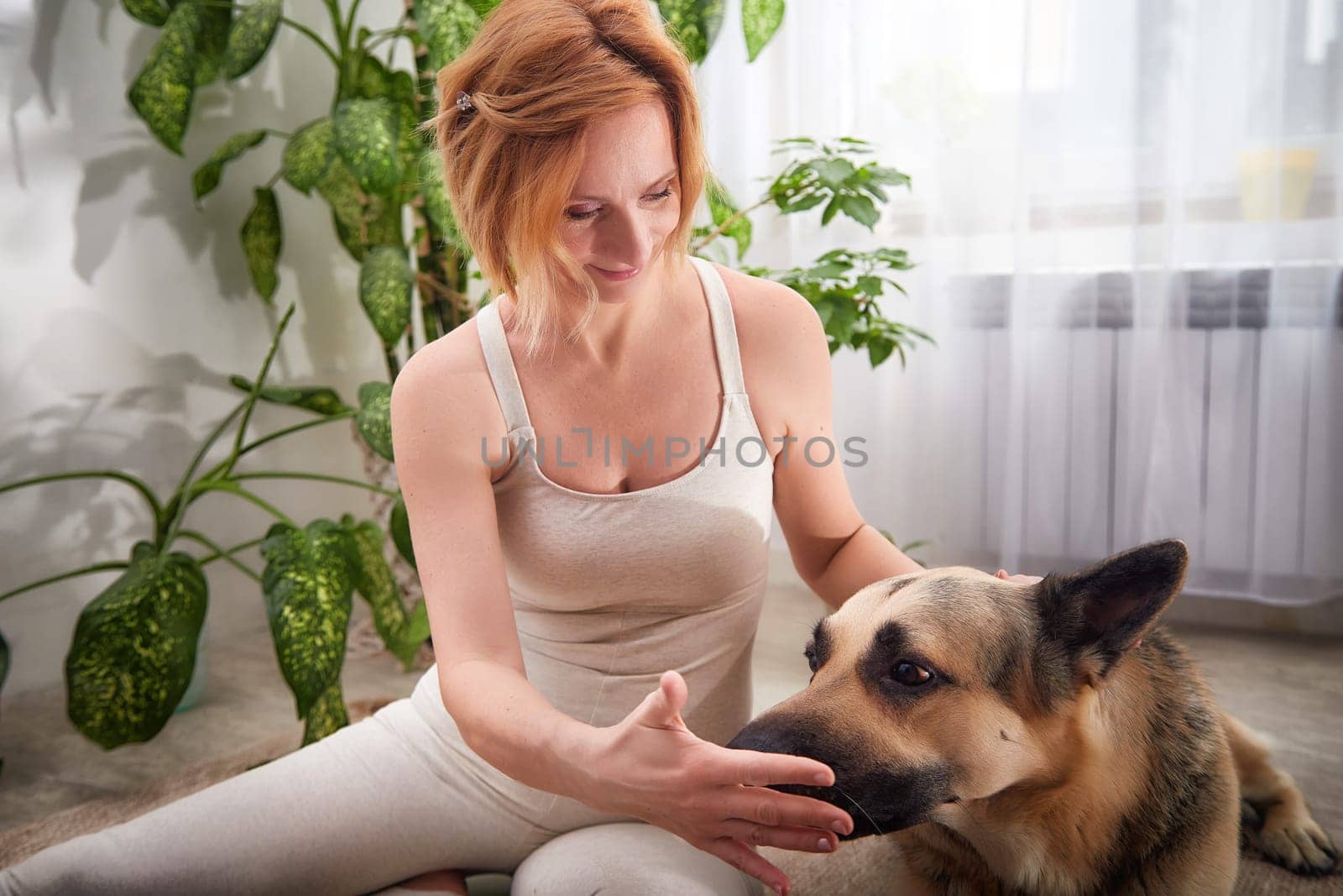 A woman practices yoga in a well-lit room surrounded by lush plants, gently interacting with her dog to emphasize a healthy lifestyle.
