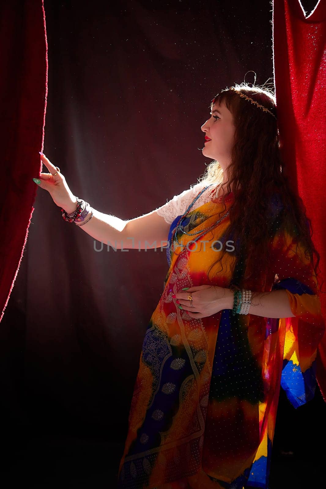 A mature woman in a colorful sari poses gracefully, highlighting her style against a dramatic backdrop, embodying a blend of culture and modernity.