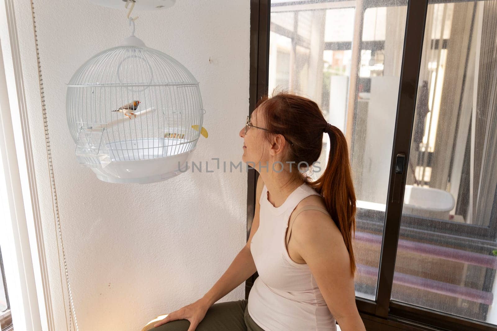 Woman admiring her zebra finch resting in its hanging cage, enjoying a peaceful moment at home