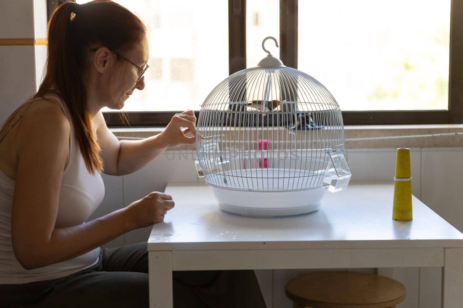 Woman taking care of her pet bird, feeding it in its cage