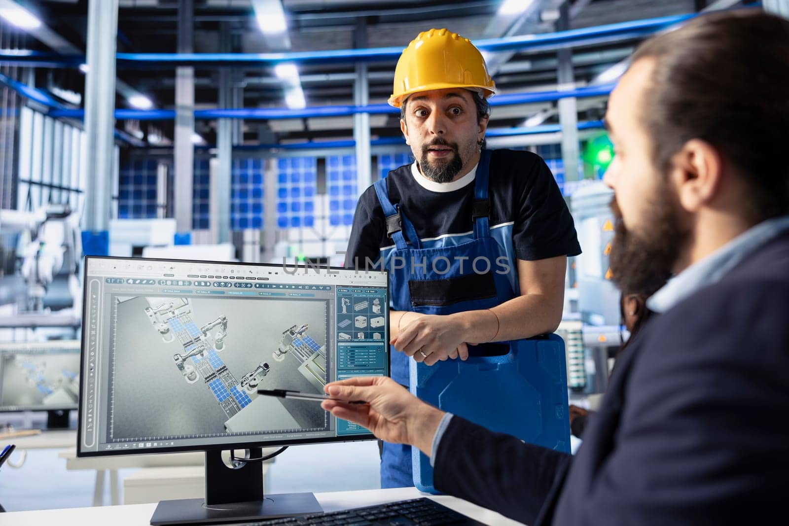 Manager in photovoltaics factory talking with worker, diagnosing malfunctioning systems, pointing to PC screen. Solar panels manufacturing plant experts doing brainstorming to reduce downtime