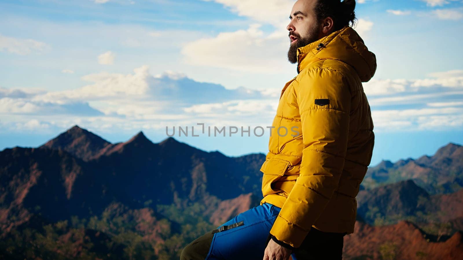 Adventure seeker gazes at the valley and mountain peaks ahead, feeling the freedom of the open wilderness. Young man fully equipped enjoying high altitude outdoor exploration. Camera A.