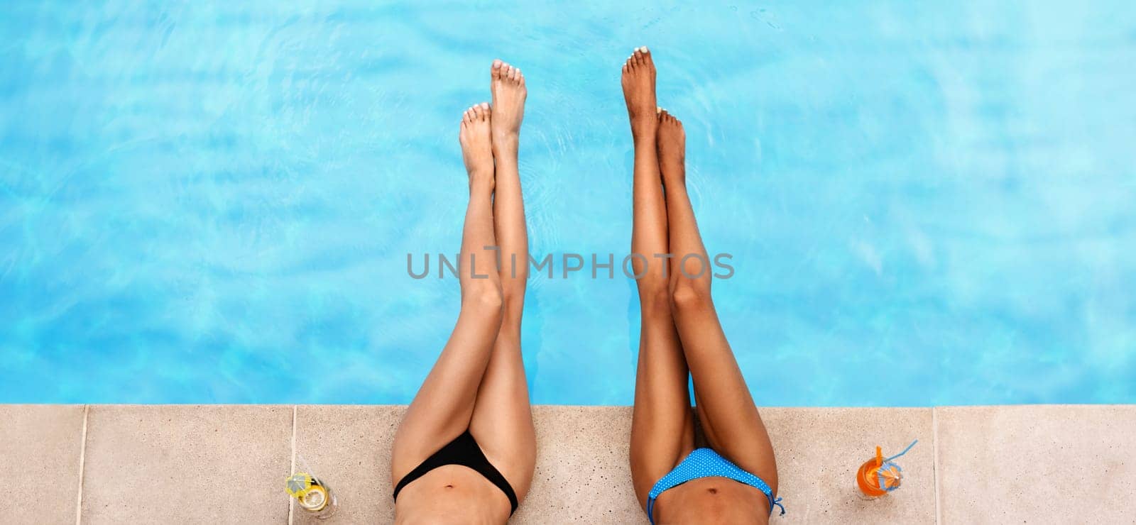 Top view of young female friends sunbathing by poolside with fresh cocktails, closeup of legs. Copy space. Panorama