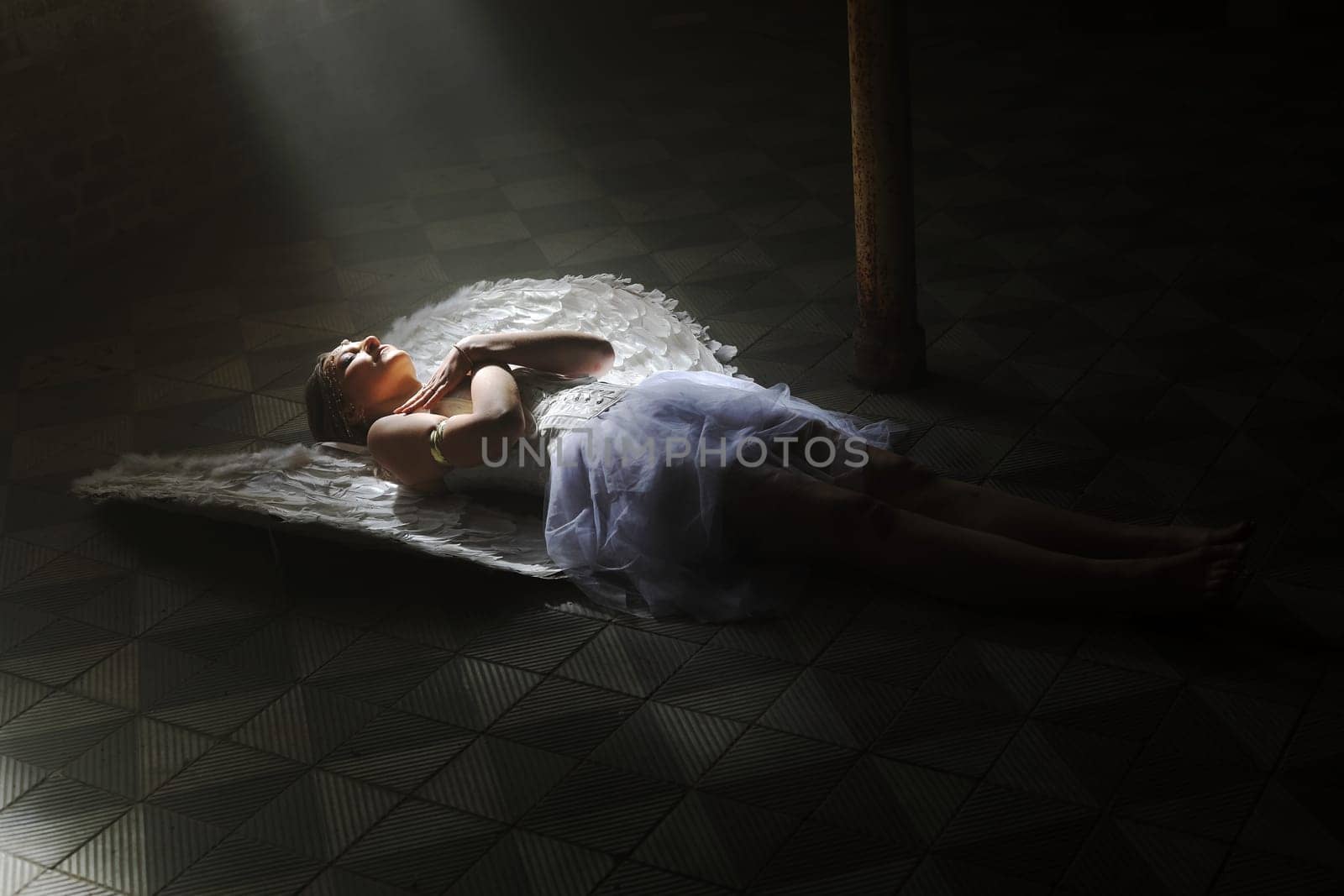 A woman dressed as an angel lies on the floor in a beam of light