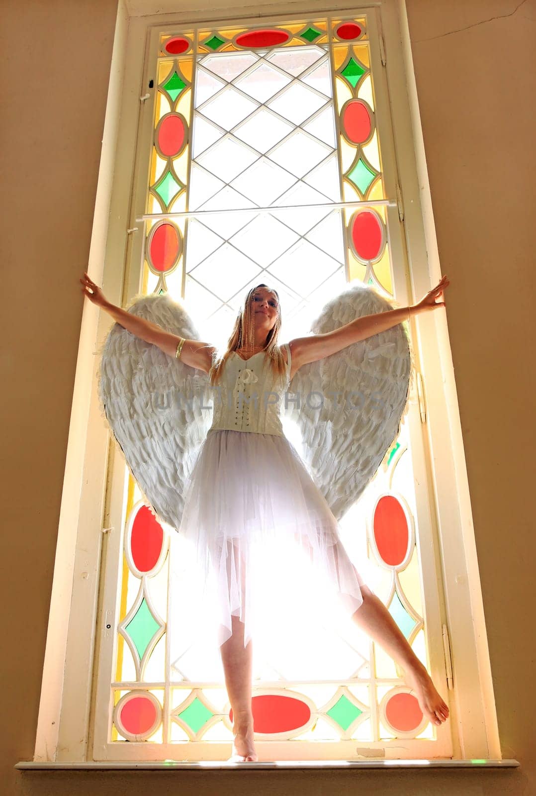 A woman dressed as an angel against the light in a colorful window