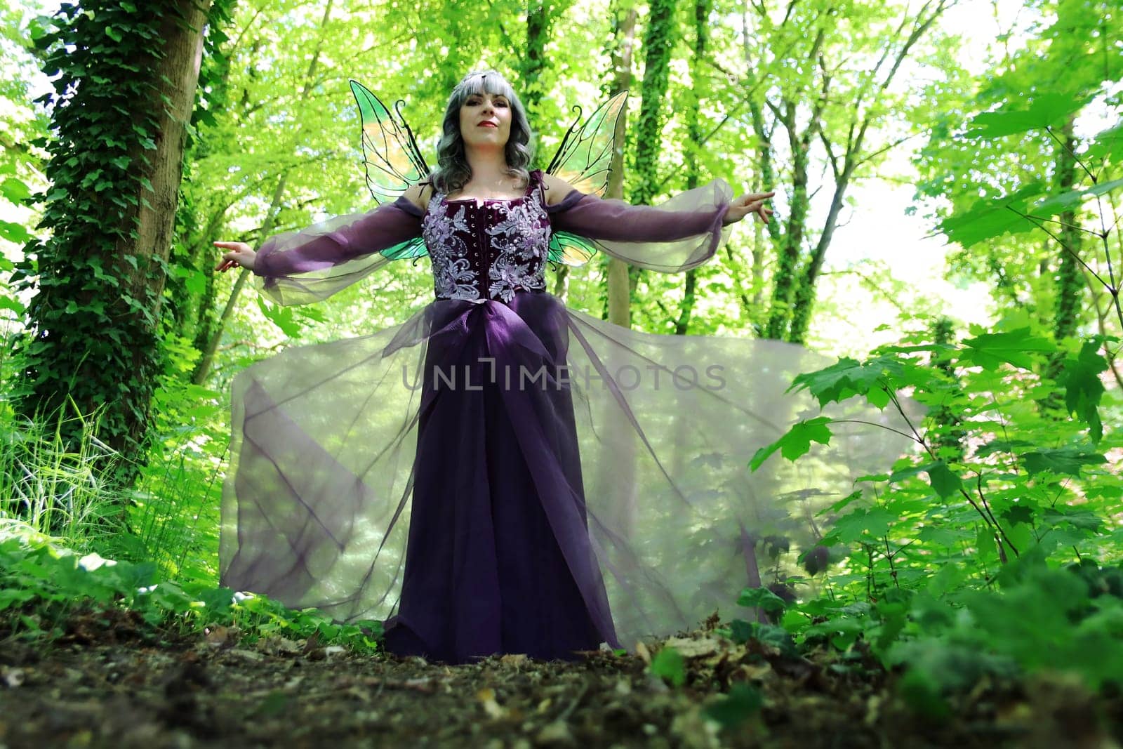 A beautiful elf with wings and a purple dress enchants a forest
