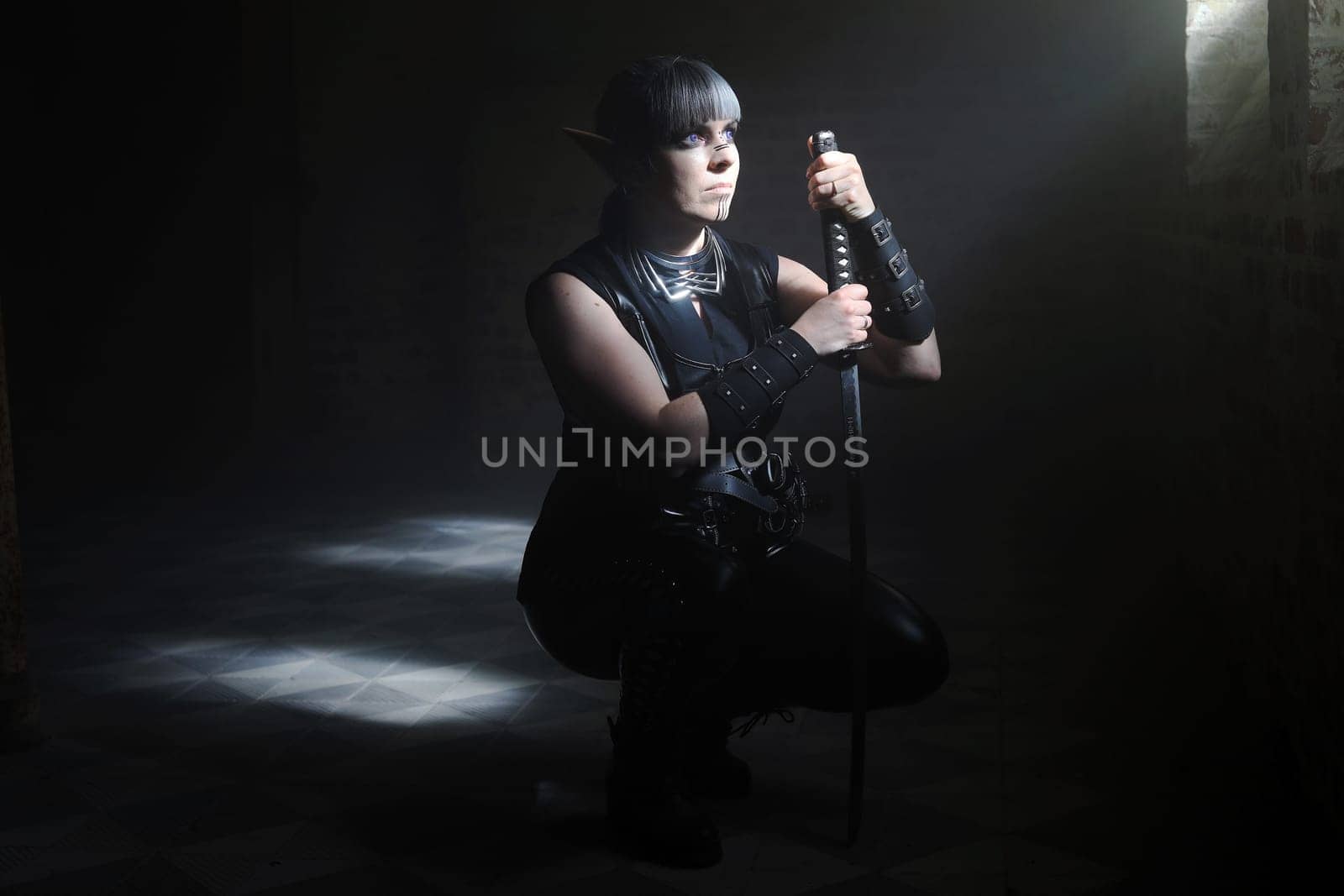 A woman disguised as a dark elf with a sword waits in the beam of light in a crypt