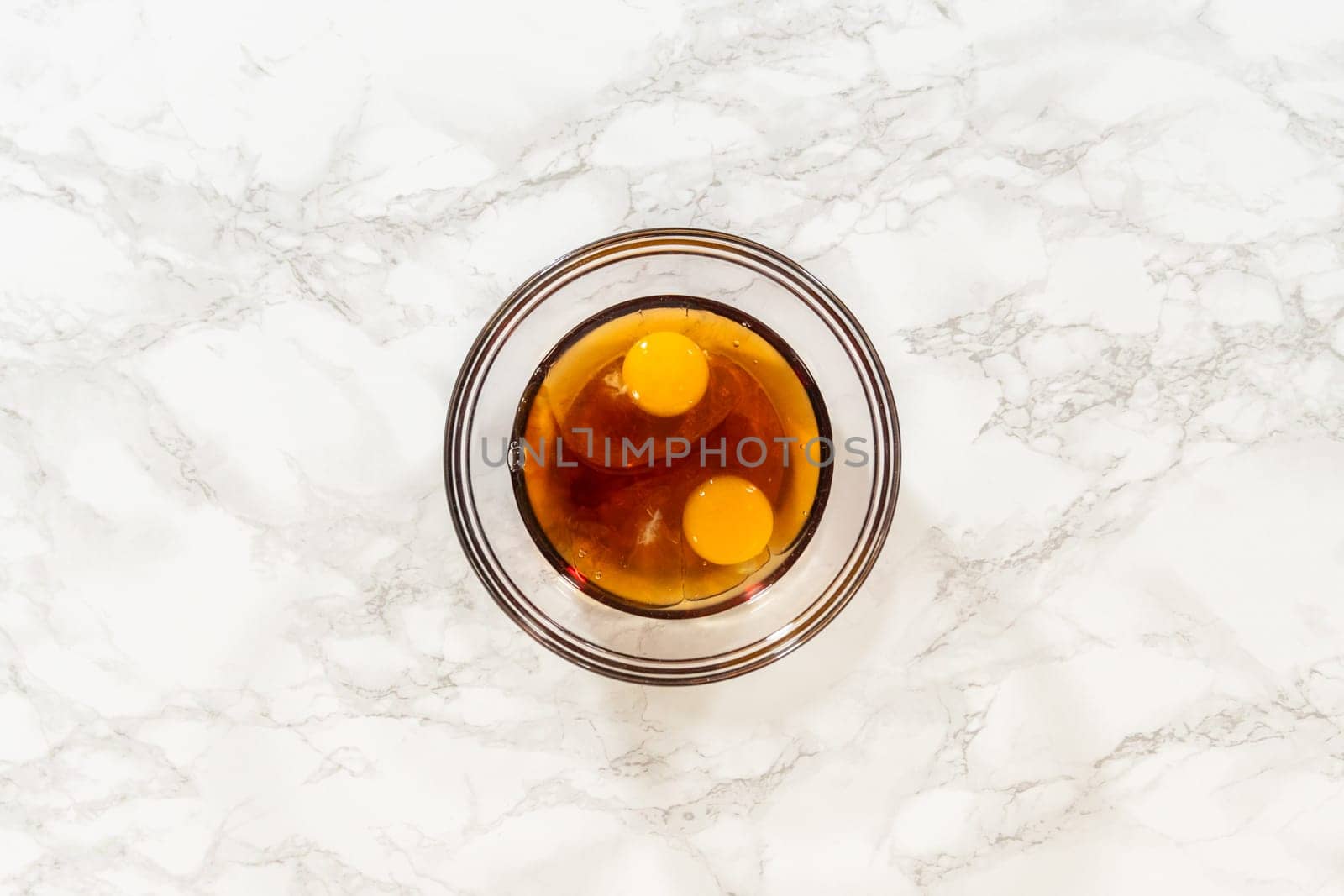 Overhead view of a glass bowl with two eggs and maple syrup for Chocolate Ginger Sugar Cookie Dough, ready to be mixed into the dough.