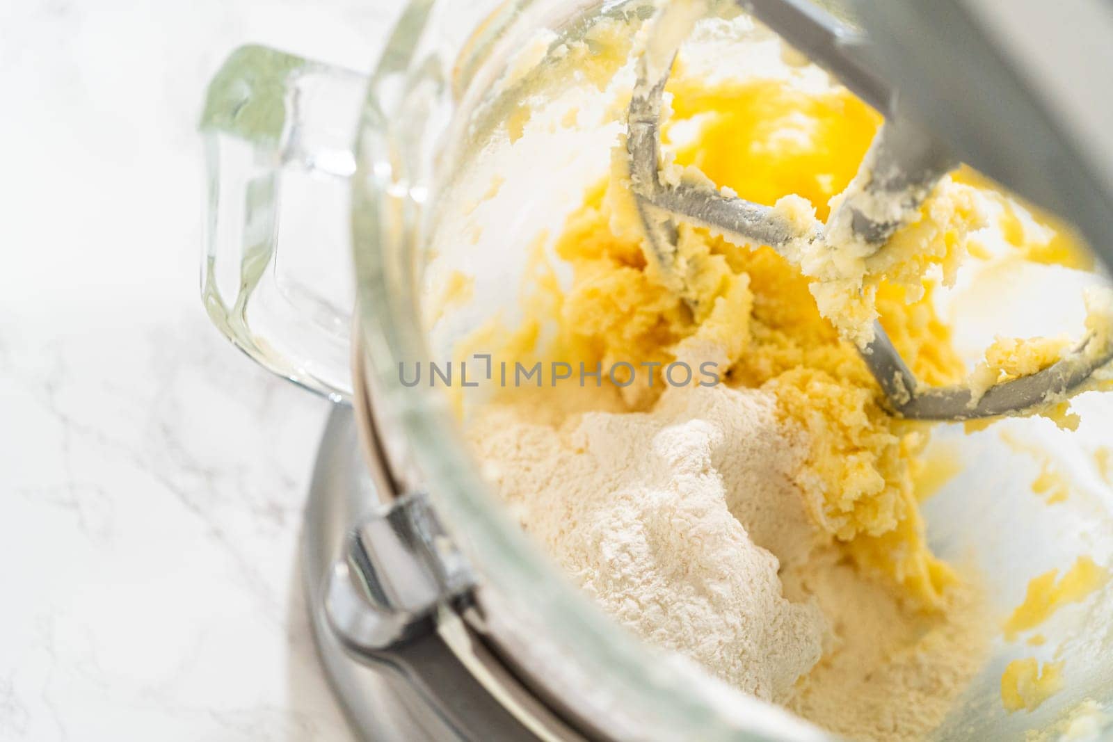 Close-up view of the stand mixer as dry ingredients are added to the wet mixture for Classic Sugar Cookie Dough. The flour is gently being incorporated into the butter, sugar, and eggs, creating the base for a smooth cookie dough.