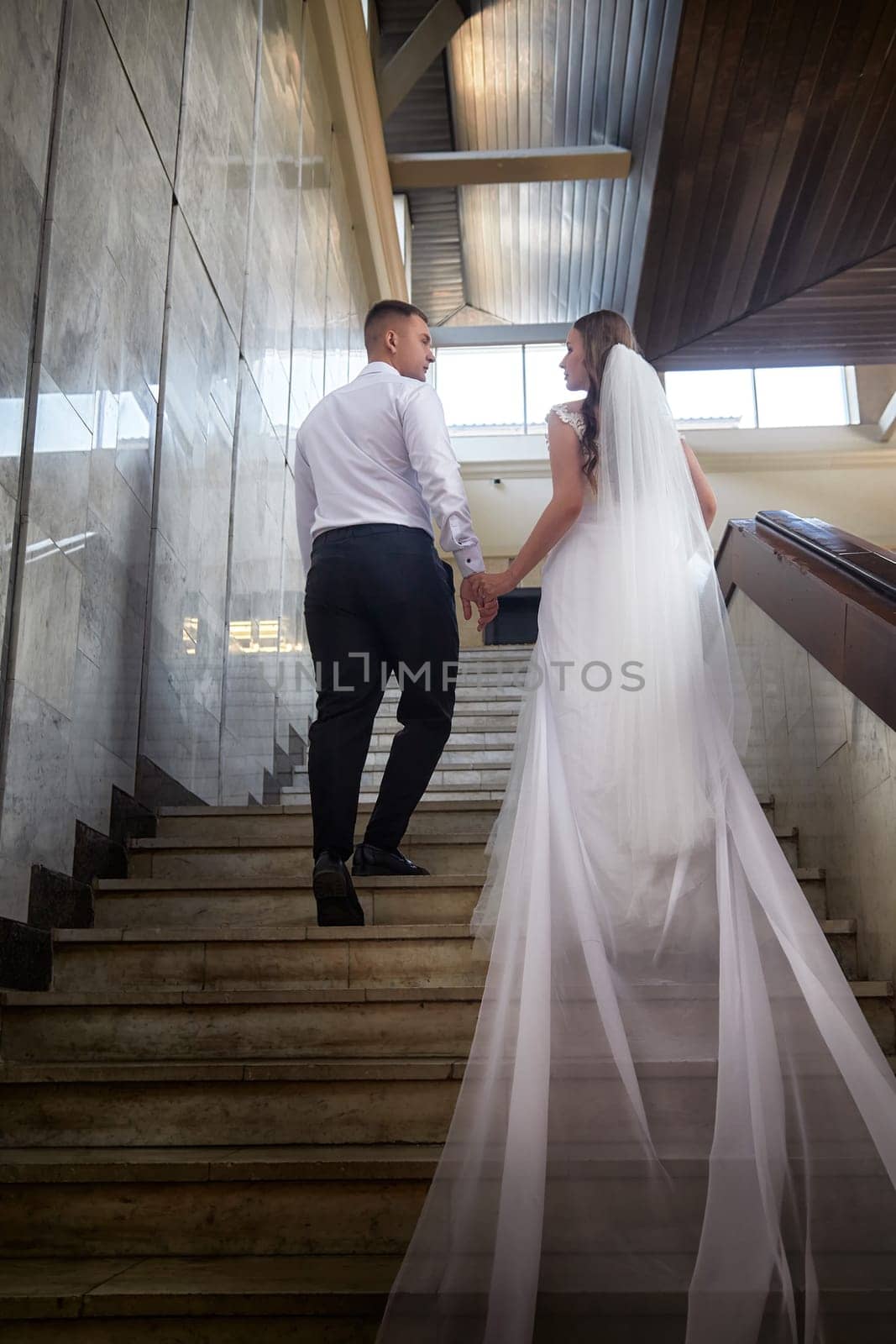A couple dressed in wedding attire ascends a staircase, symbolizing their journey together as newlyweds at their registration event.