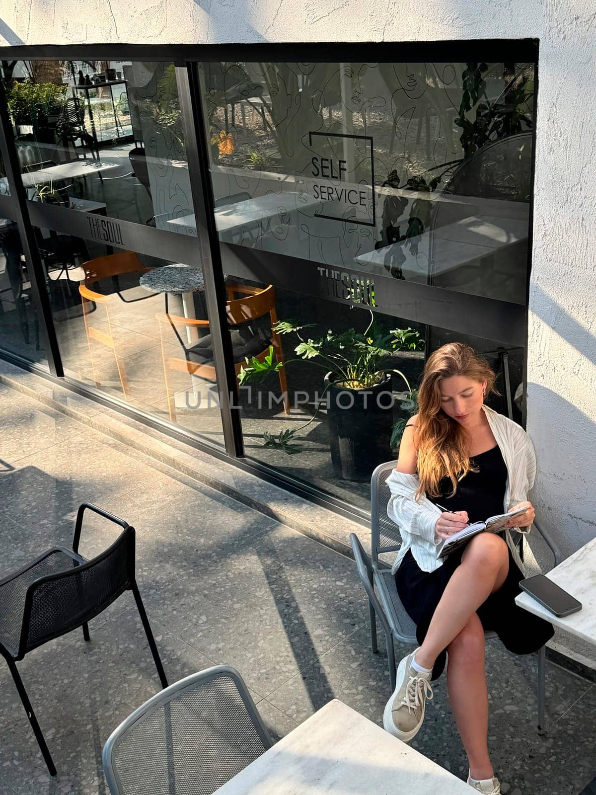 A woman reads a book while seated at a table in a stylish self-service cafe with plenty of natural light.