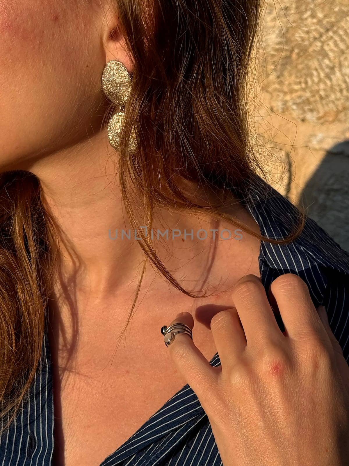 A woman is highlighting her fashionable earrings and ring while enjoying a sunny moment outdoors.