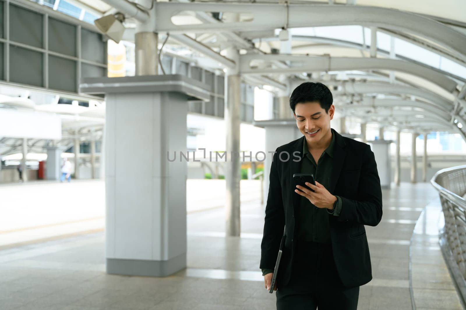 Young male executive walking through a modern walkway and checking his smartphone.