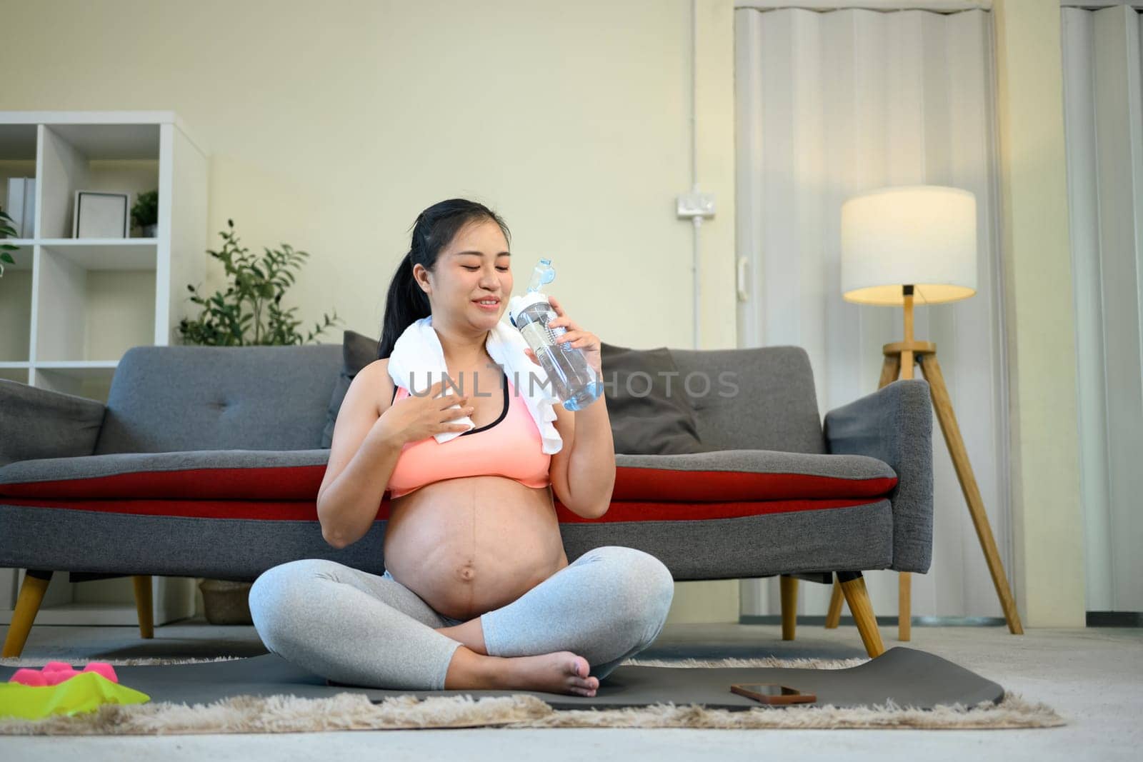 Pregnant woman taking a water break after exercising at home..