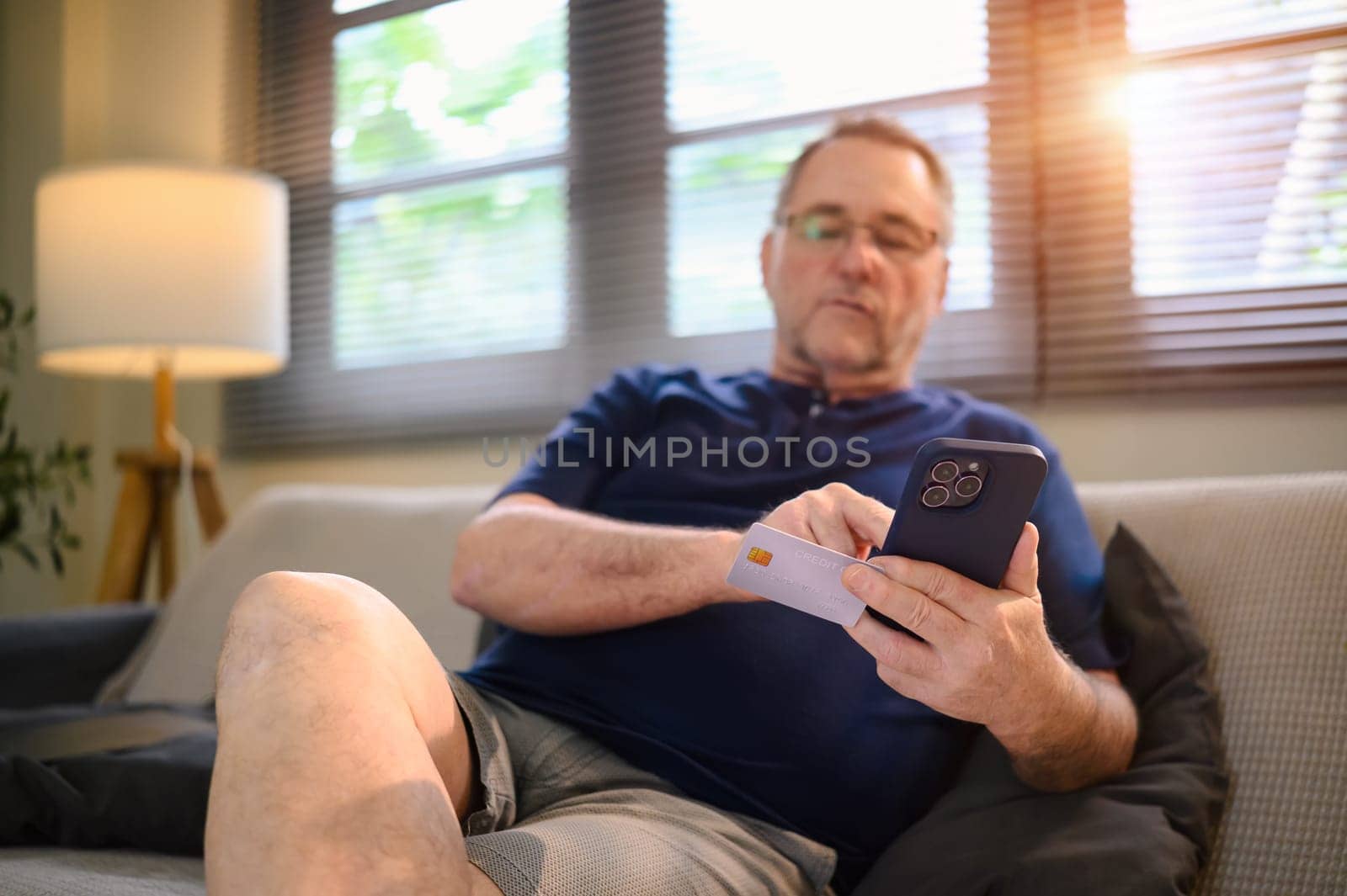 Senior man making an online payment using credit card and smartphone at home.