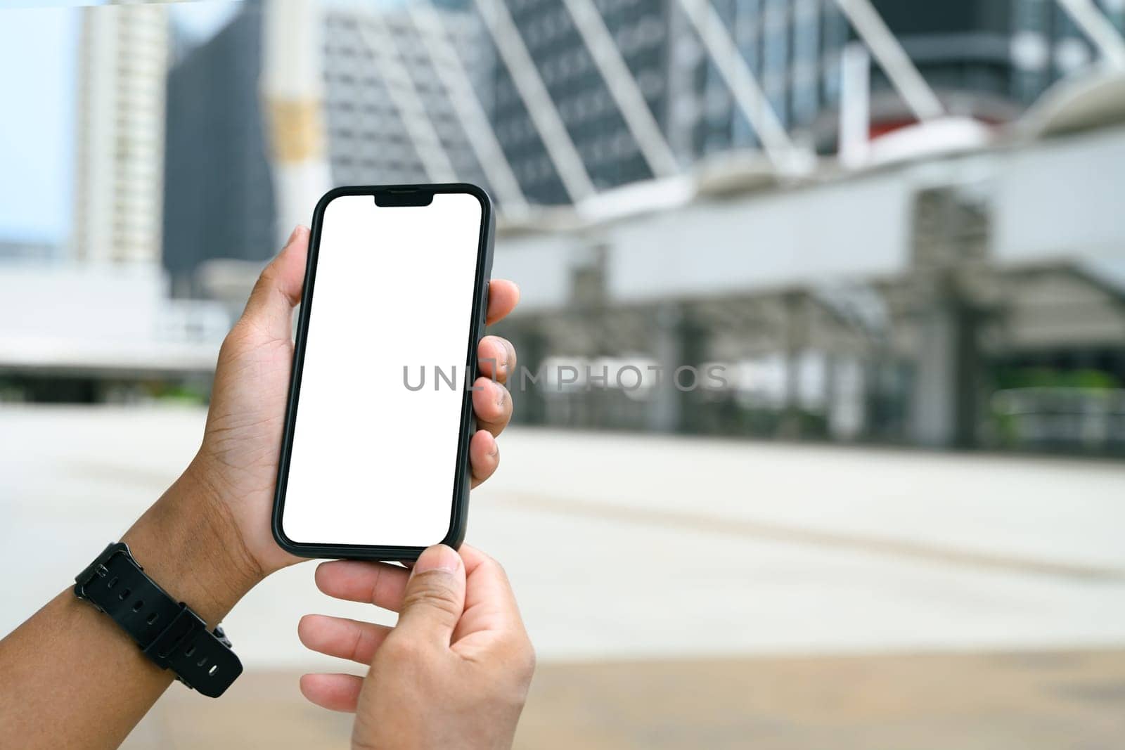 Hands holding smartphone with blank white screen in an urban cityscape.