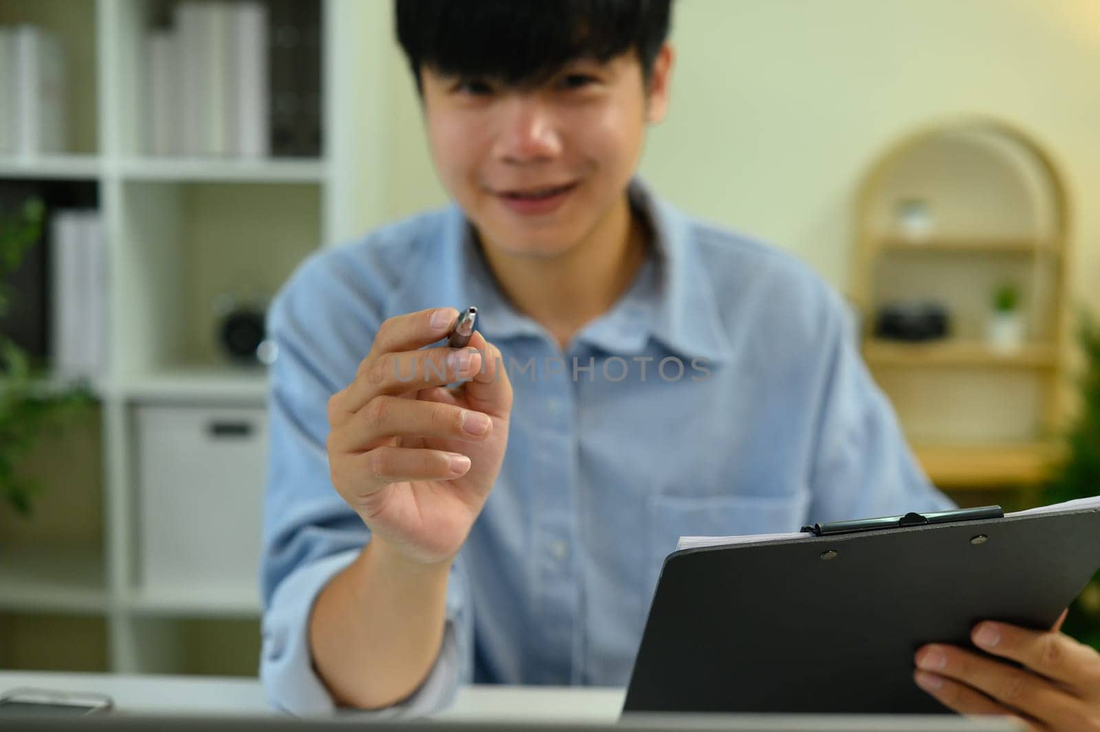 Close up of man extending a pen toward the camera, symbolizing signing or approval.