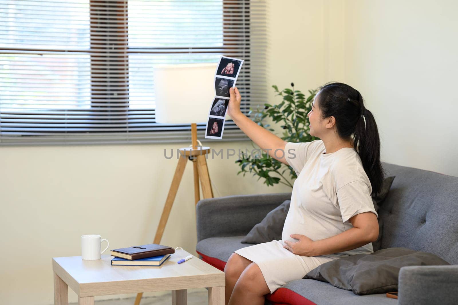 Happy pregnant woman admiring sonogram photos and gently touching her belly.