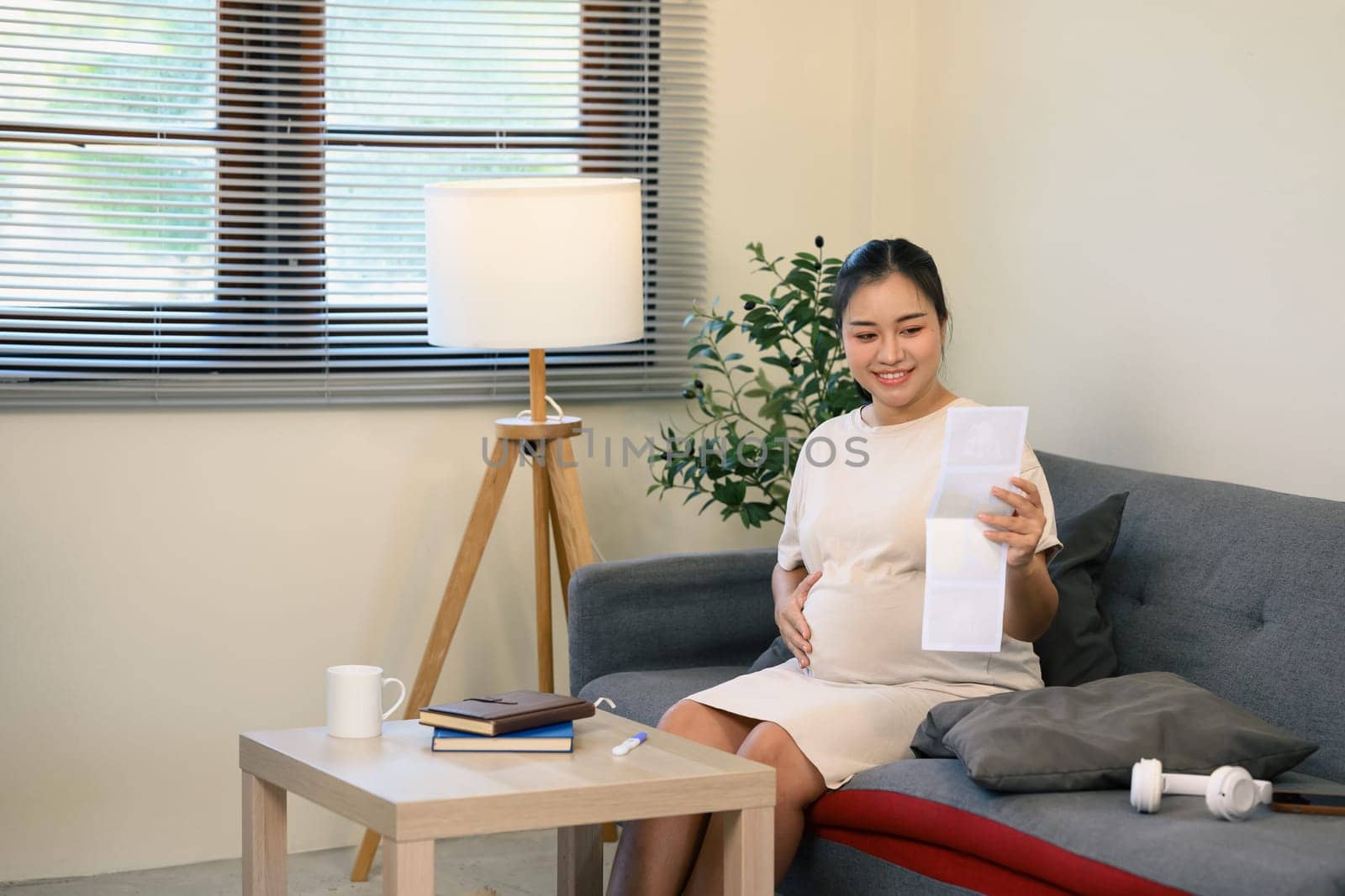 Happy pregnant woman admiring sonogram photos and gently touching her belly.