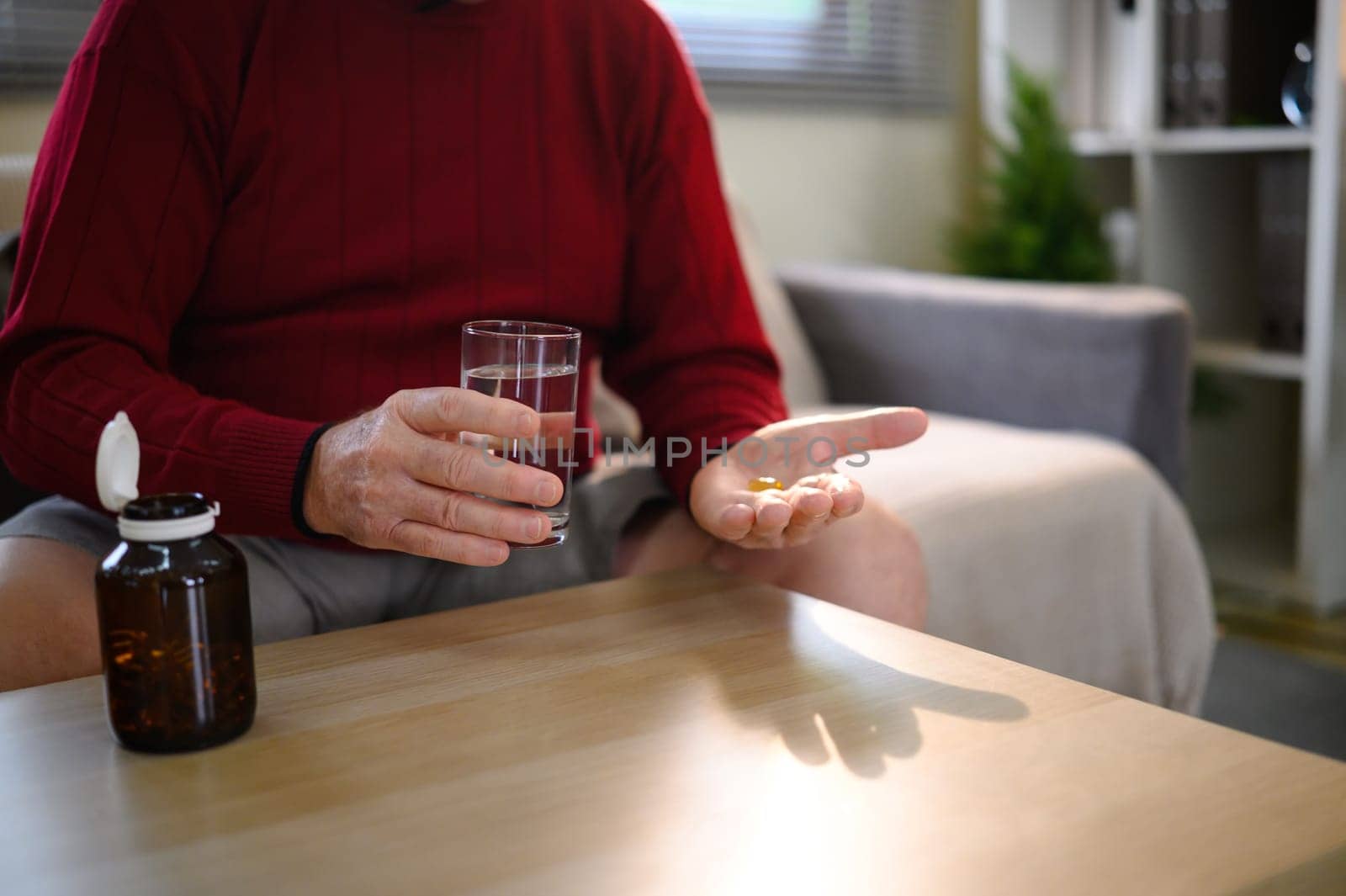 Close up of senior man holding pills and a glass of water near a pill bottle.