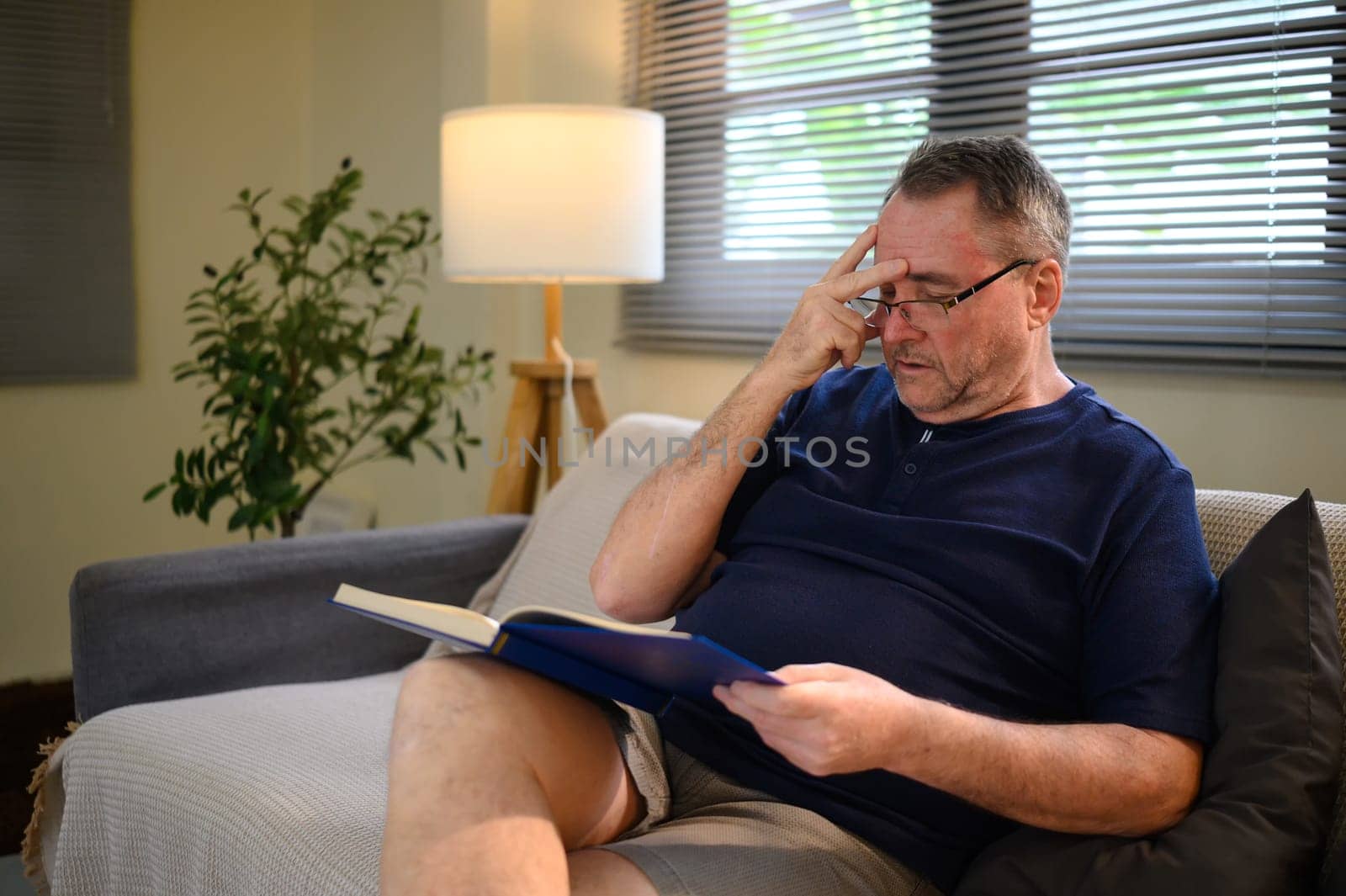 Middle aged man holding a book and showing signs of mental fatigue or difficulty concentrating.