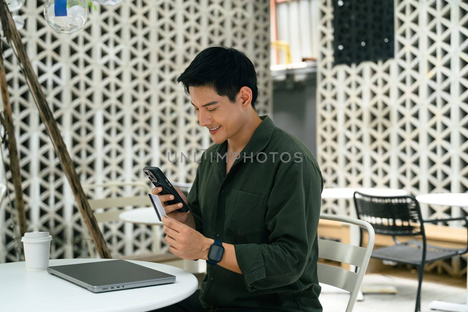 Adult asian man using mobile phone and credit card to complete a transaction.