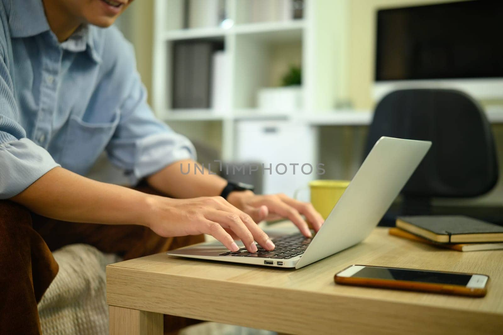 Close up of man working on laptop at home, focusing on hands typing on keyboard.