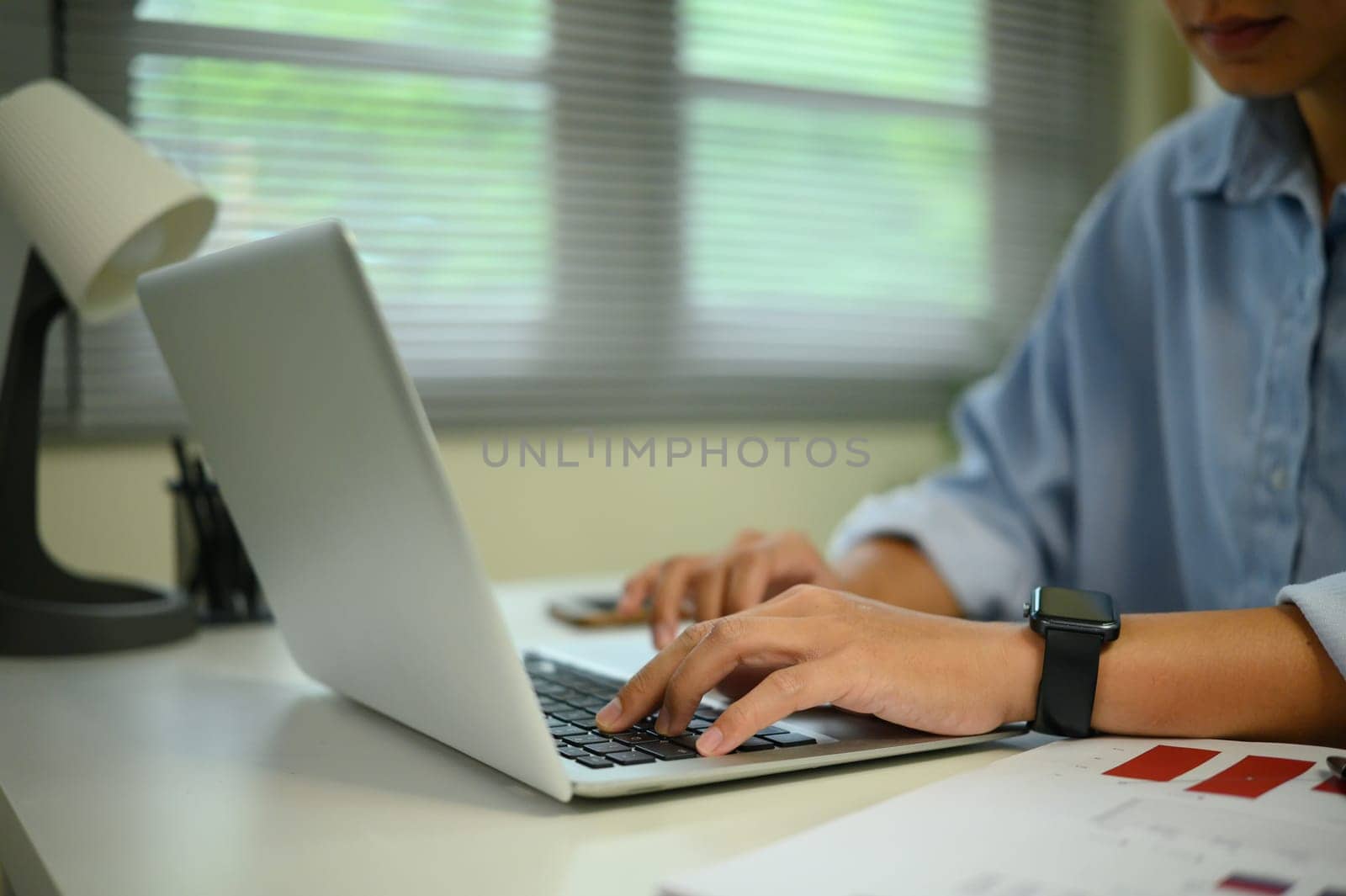 Close up of hands typing on a laptop in a bright home office with modern decor.