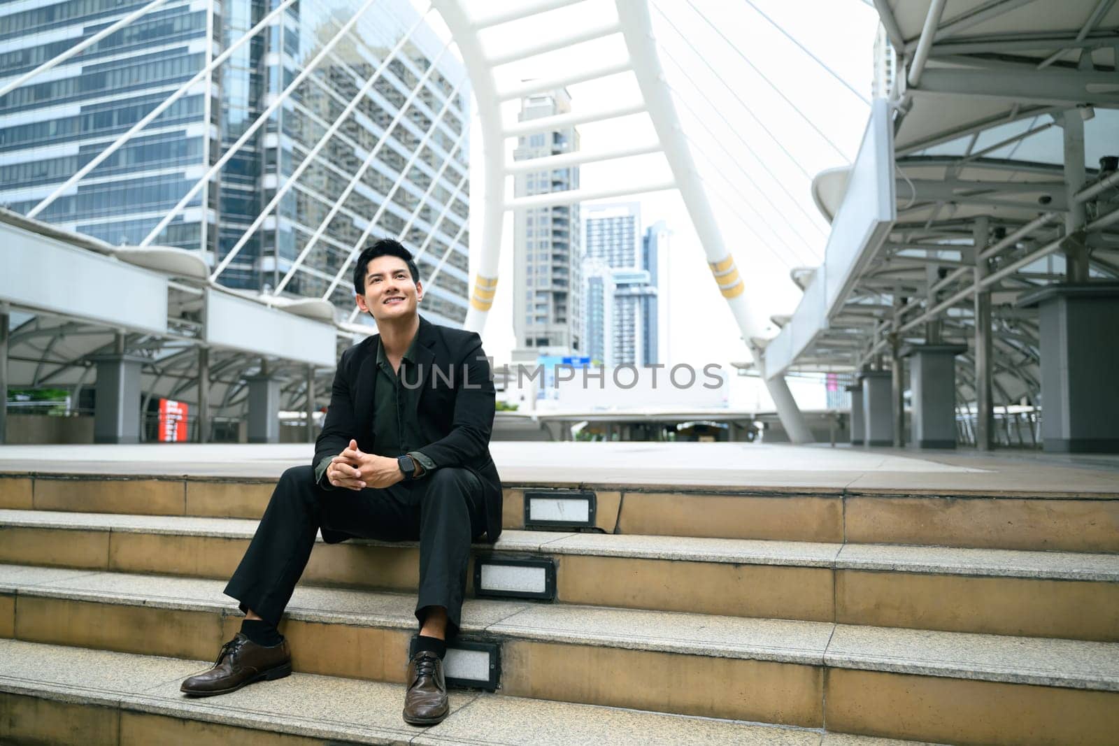 Confident businessman sitting on outdoor steps in a modern city.