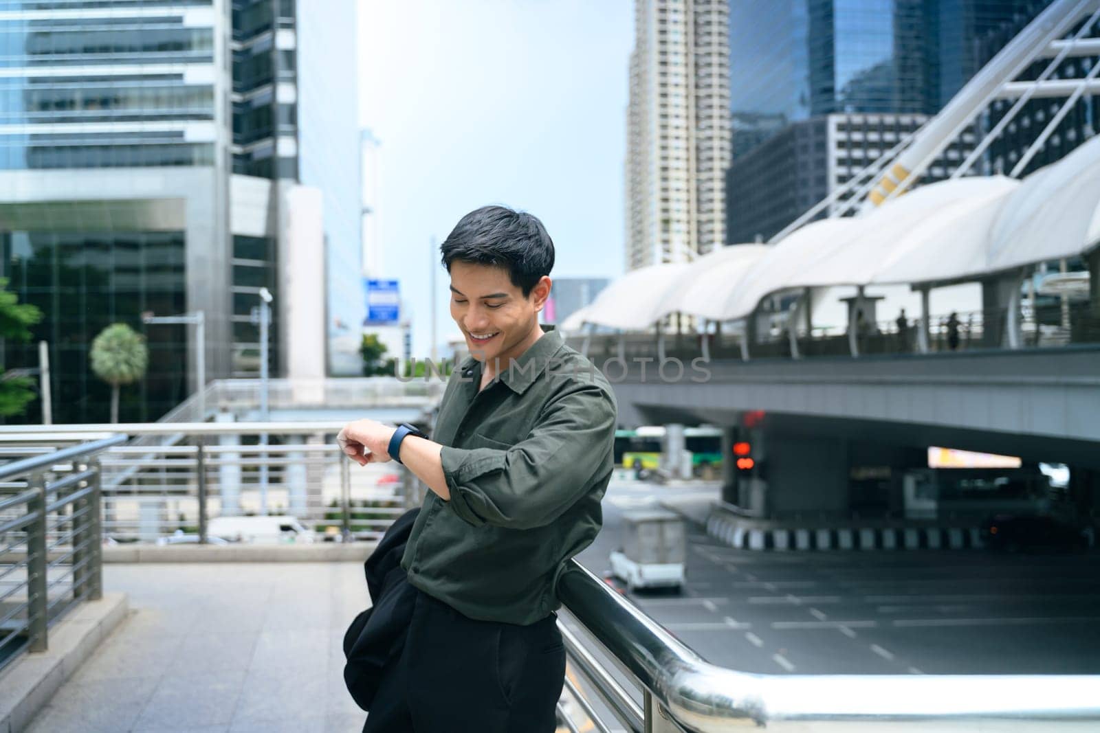 Adult businessman standing on an urban walkway, checking his smartwatch.
