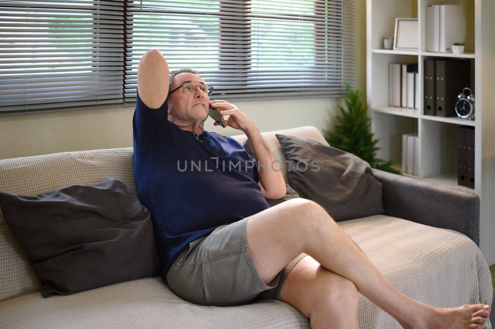 Senior man talking on the phone at home with a worried expression.