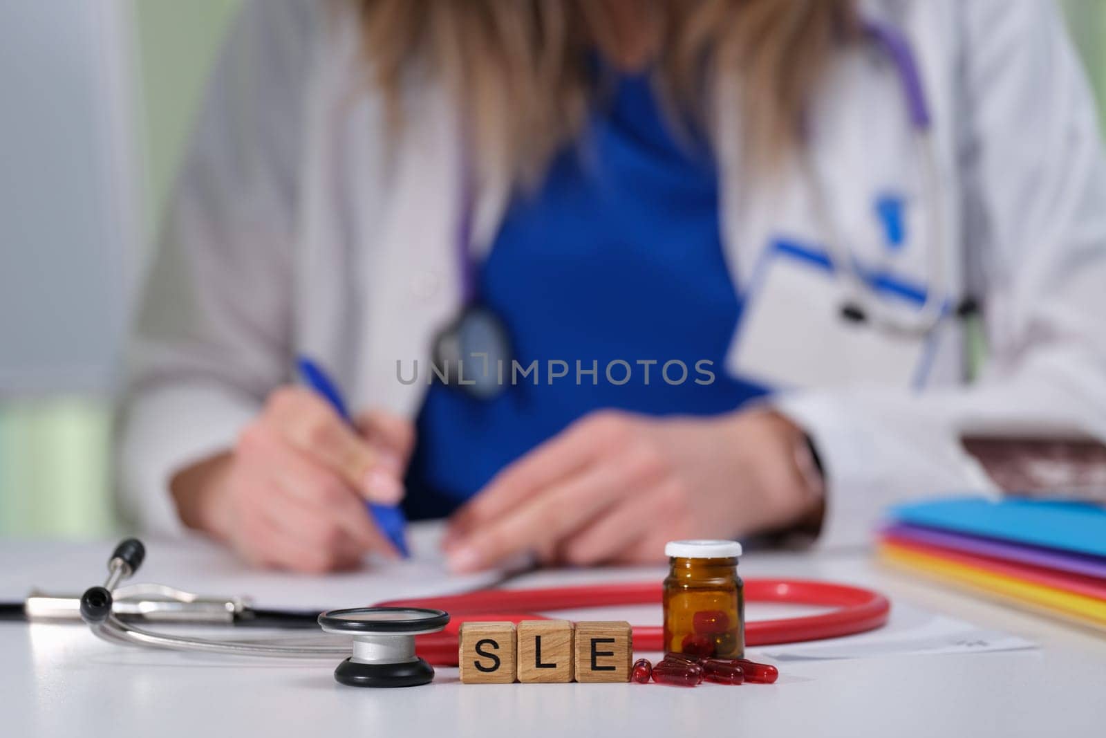 A healthcare professional is diligently writing notes while a stethoscope and SLE medication are placed on the table