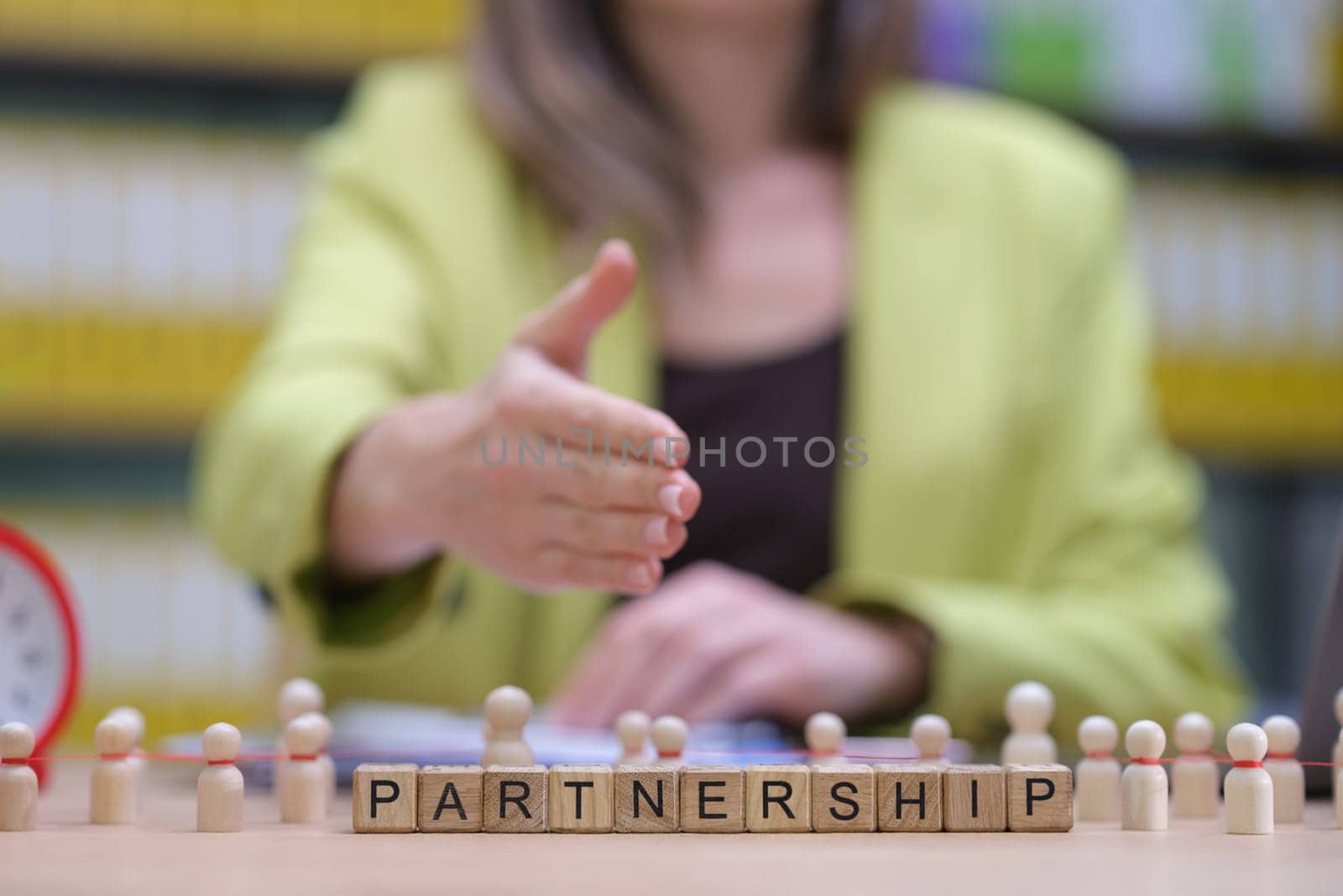 A handshake gesture symbolizing partnership, surrounded by wooden figures and letters spelling 'PARTNERSHIP'.